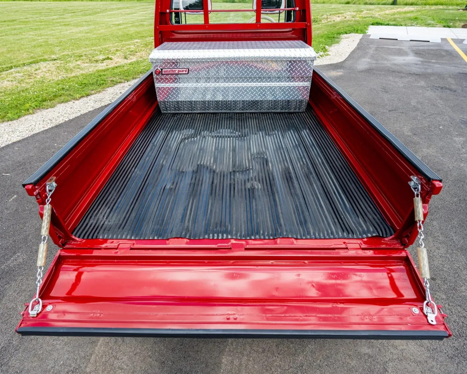 Red pickup truck bed with black ribbed liner and a silver diamond-plate Weather Guard toolbox near the cab.