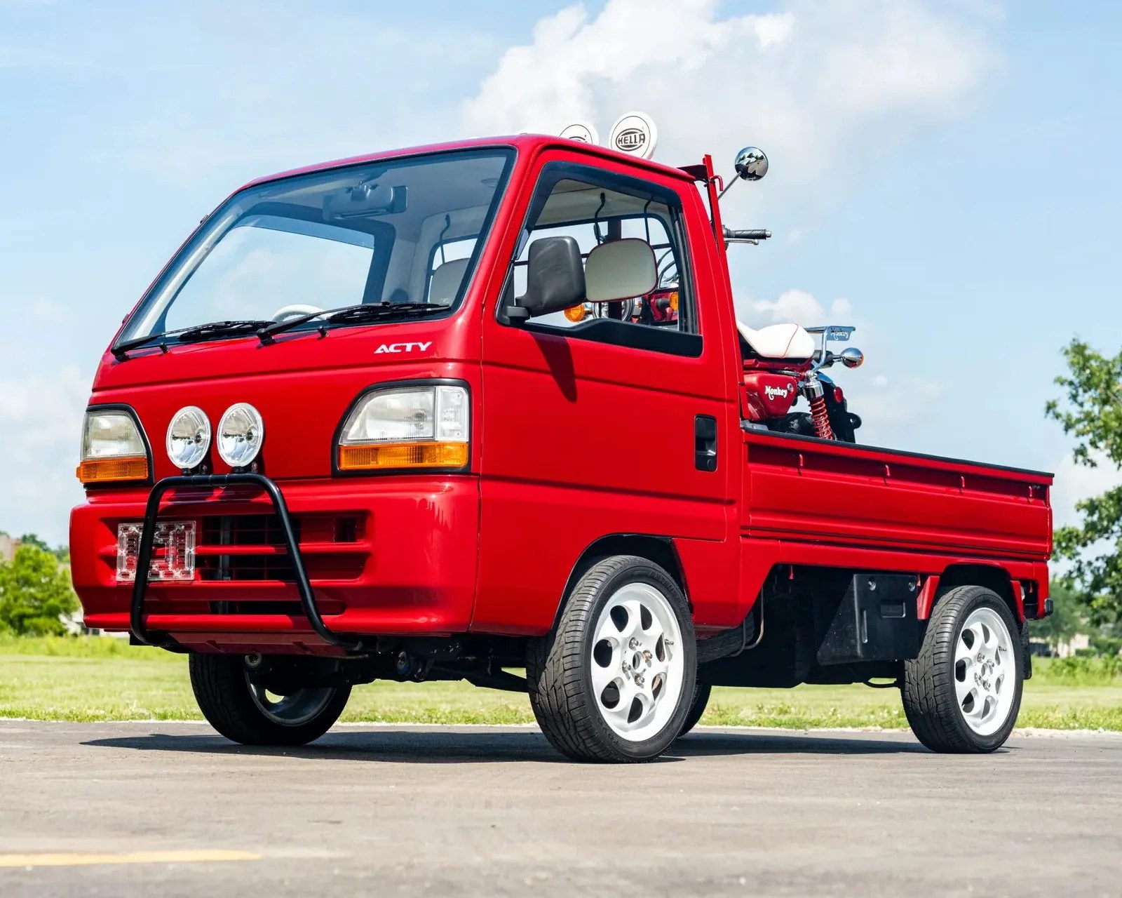 Red Honda Acty mini truck with white wheels parked on pavement with a motorcycle in the bed.