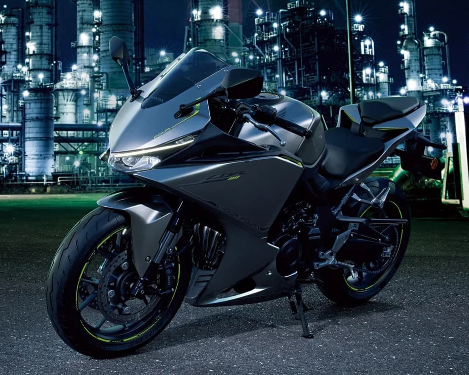 Matte gray sport motorcycle with black and neon yellow accents parked on asphalt at night with industrial buildings in the background.