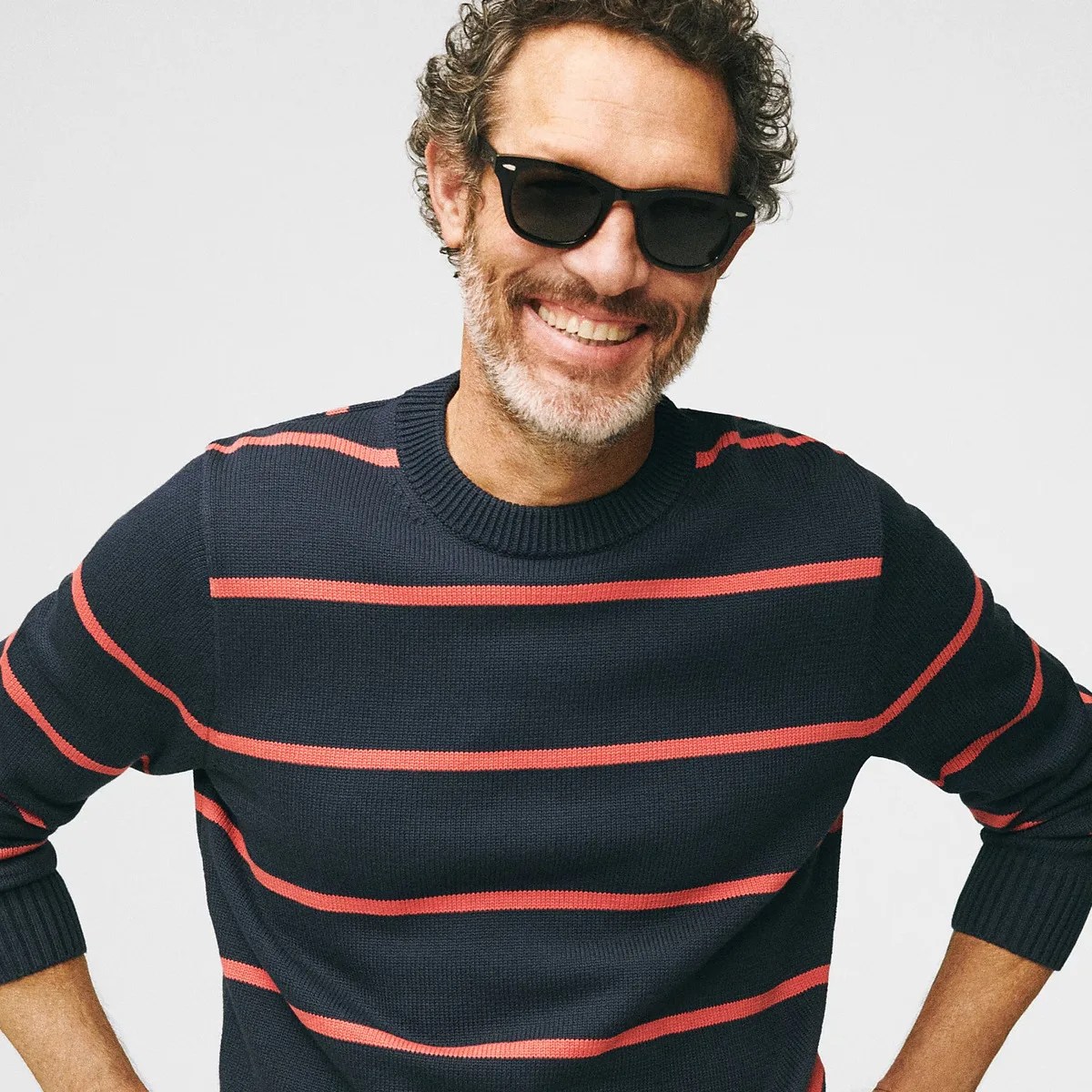 Man wearing black sunglasses and a navy blue sweater with red horizontal stripes.