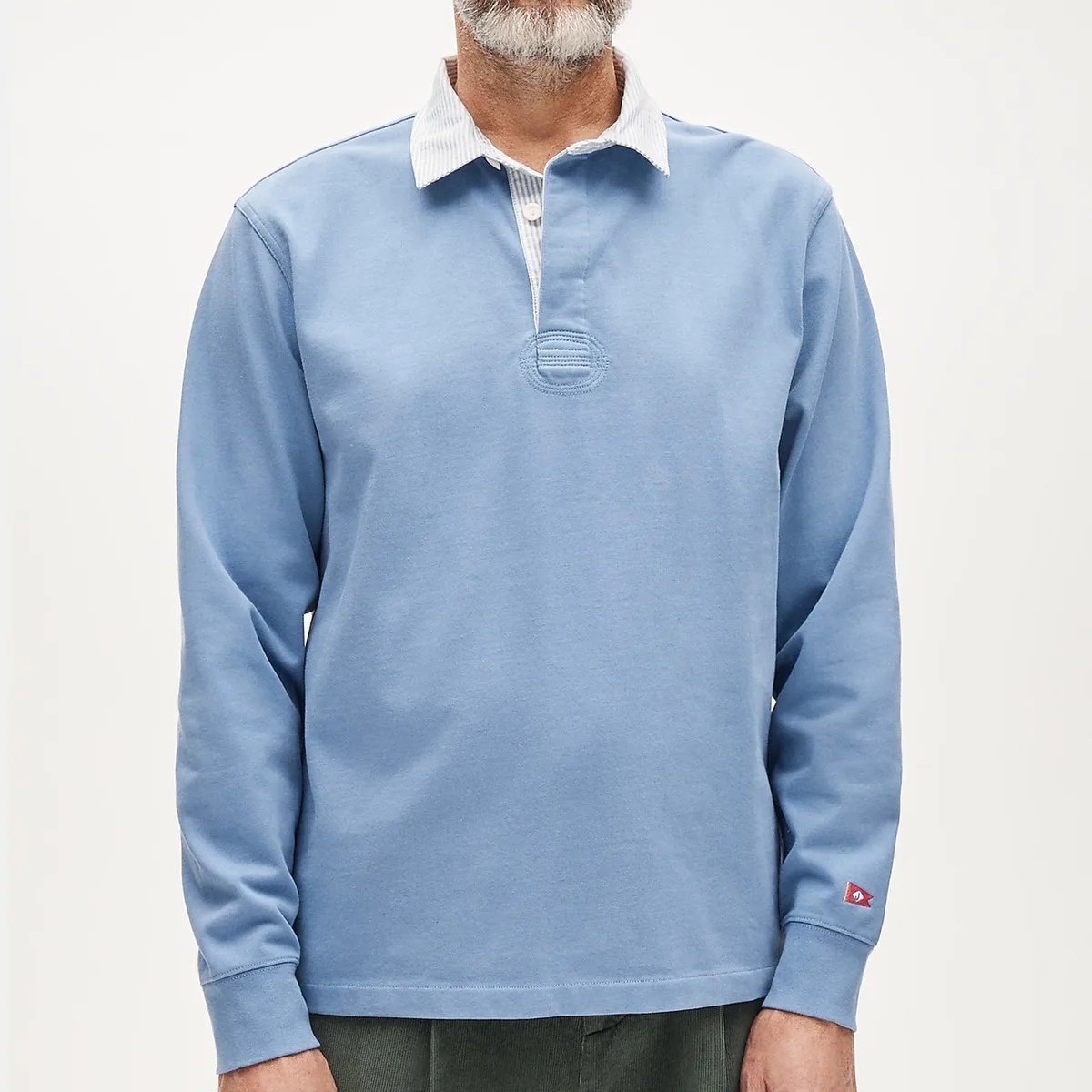 Light blue long-sleeve rugby shirt with white striped collar and small red logo patch on the cuff.