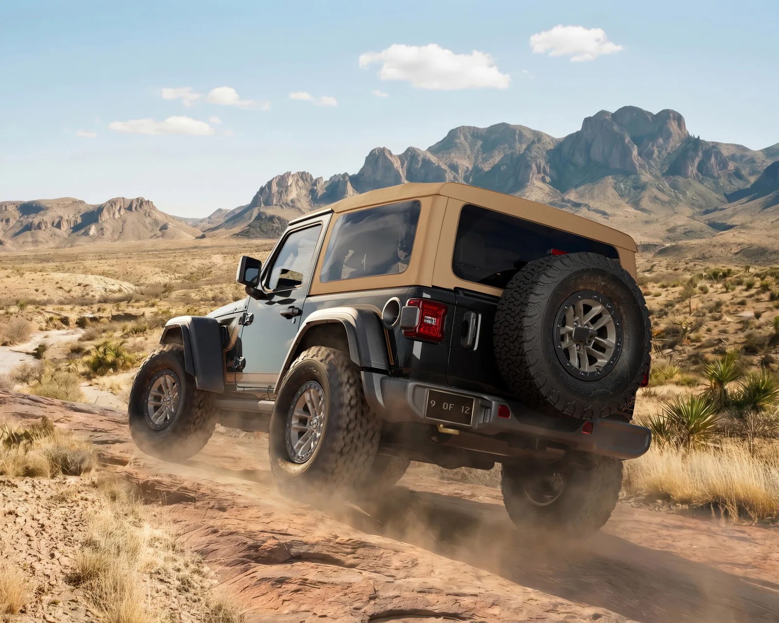 Black off-road SUV with tan soft top driving on rocky desert terrain with mountains in the background.