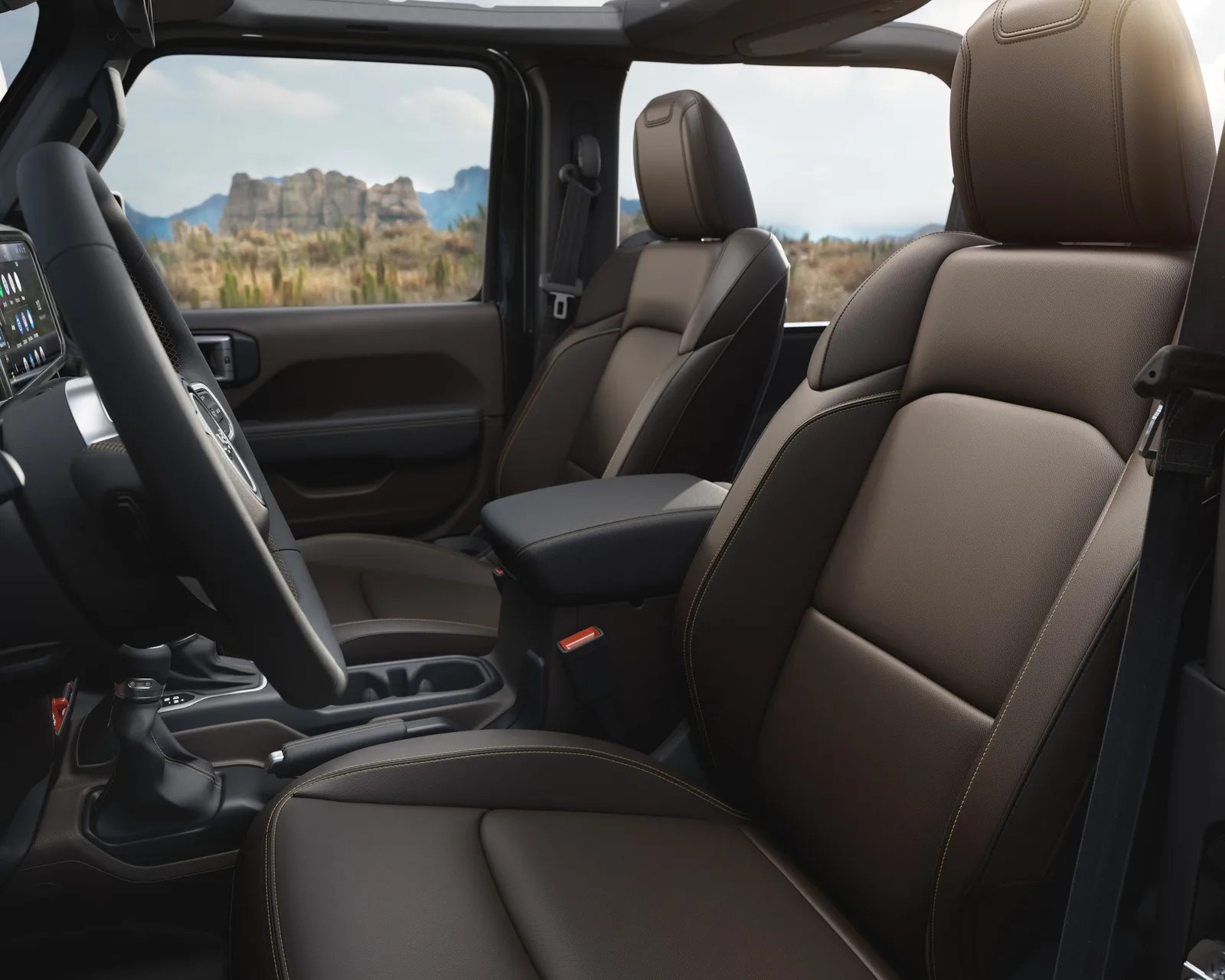 Brown leather front seats with contrast stitching inside a vehicle with a center console and visible steering wheel.