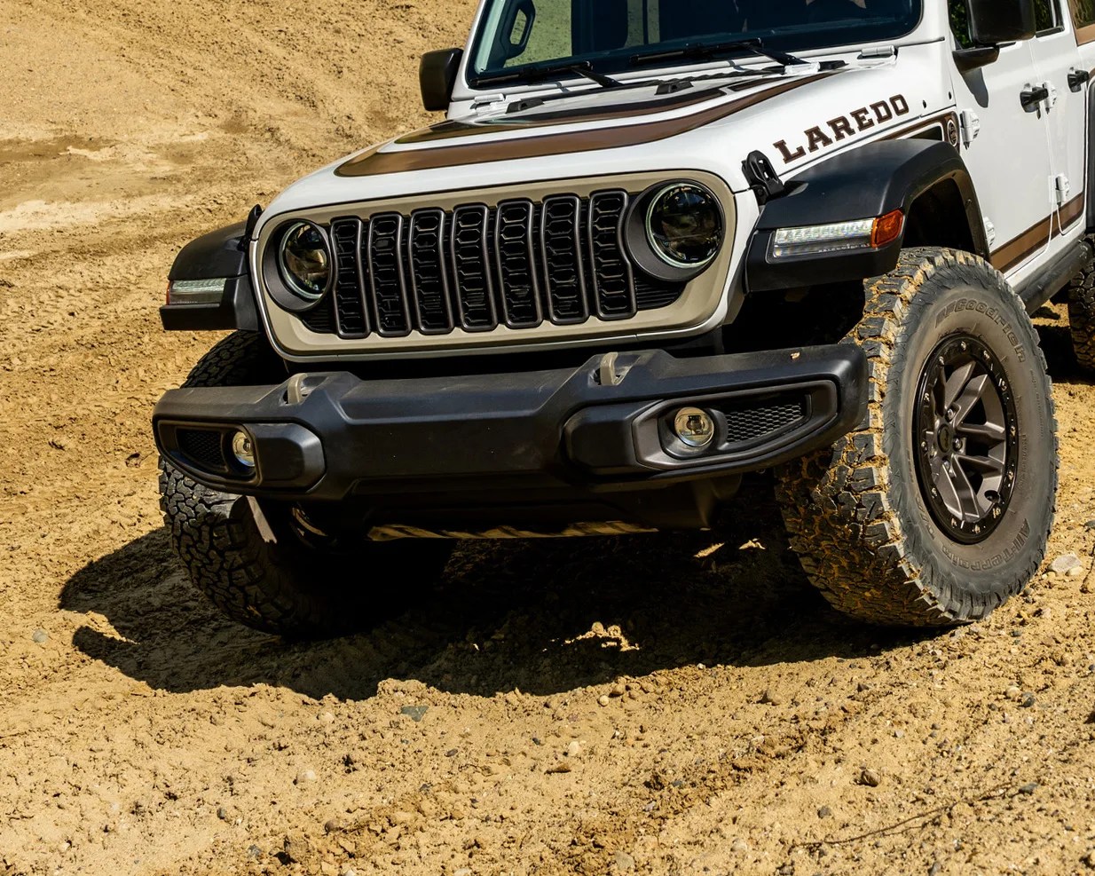 White Jeep Wrangler Laredo with brown stripes and black off-road tires on sandy terrain.