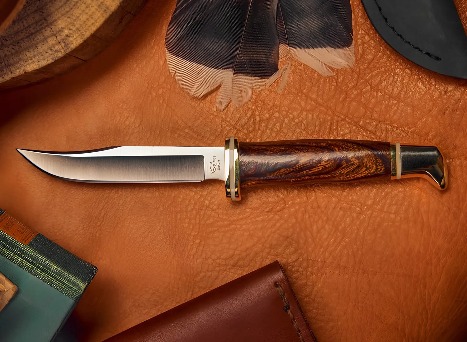 Hunting knife with polished steel blade and dark wood handle with brass accents on a textured brown leather surface.