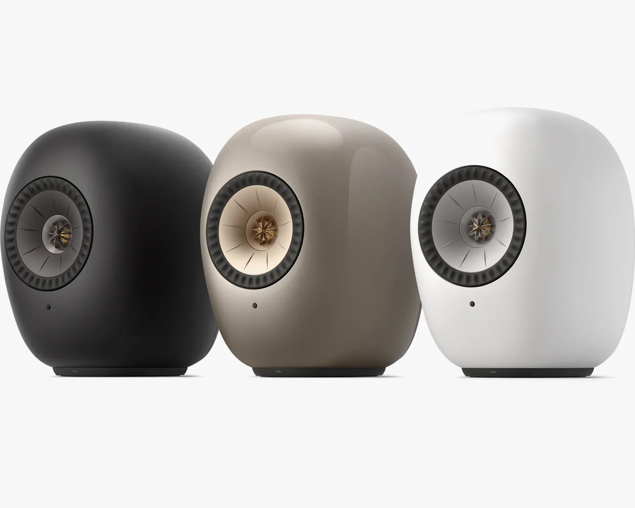 Three rounded, modern speakers in black, beige, and white with central cone drivers and textured outer rings.
