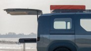 Rear side view of a blue Vantrack camper van with an open tailgate and a red rooftop tent labeled "Zelt.