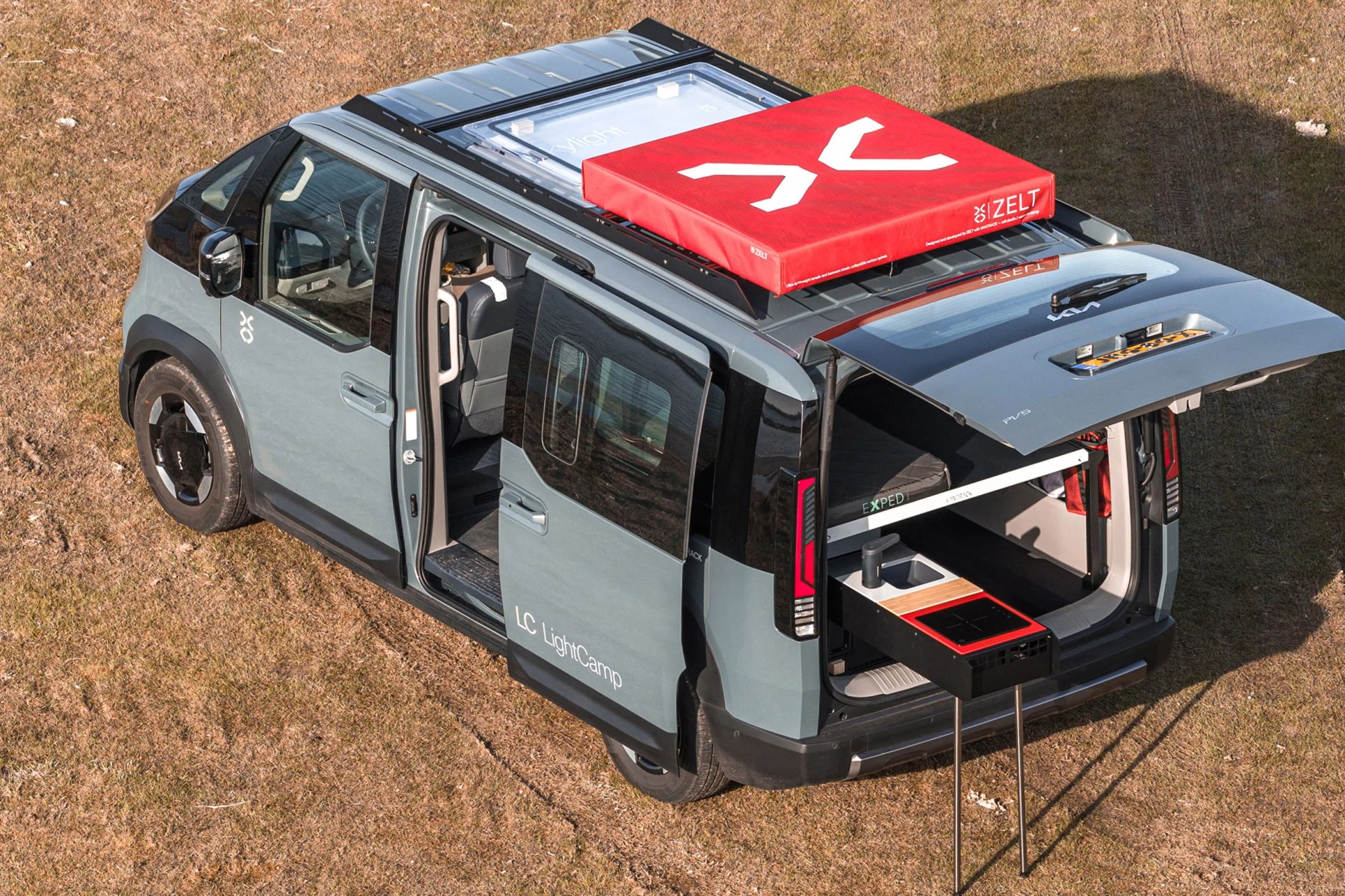 Gray compact camper van with open sliding door and rear hatch, featuring a red rooftop tent and pull-out kitchenette.