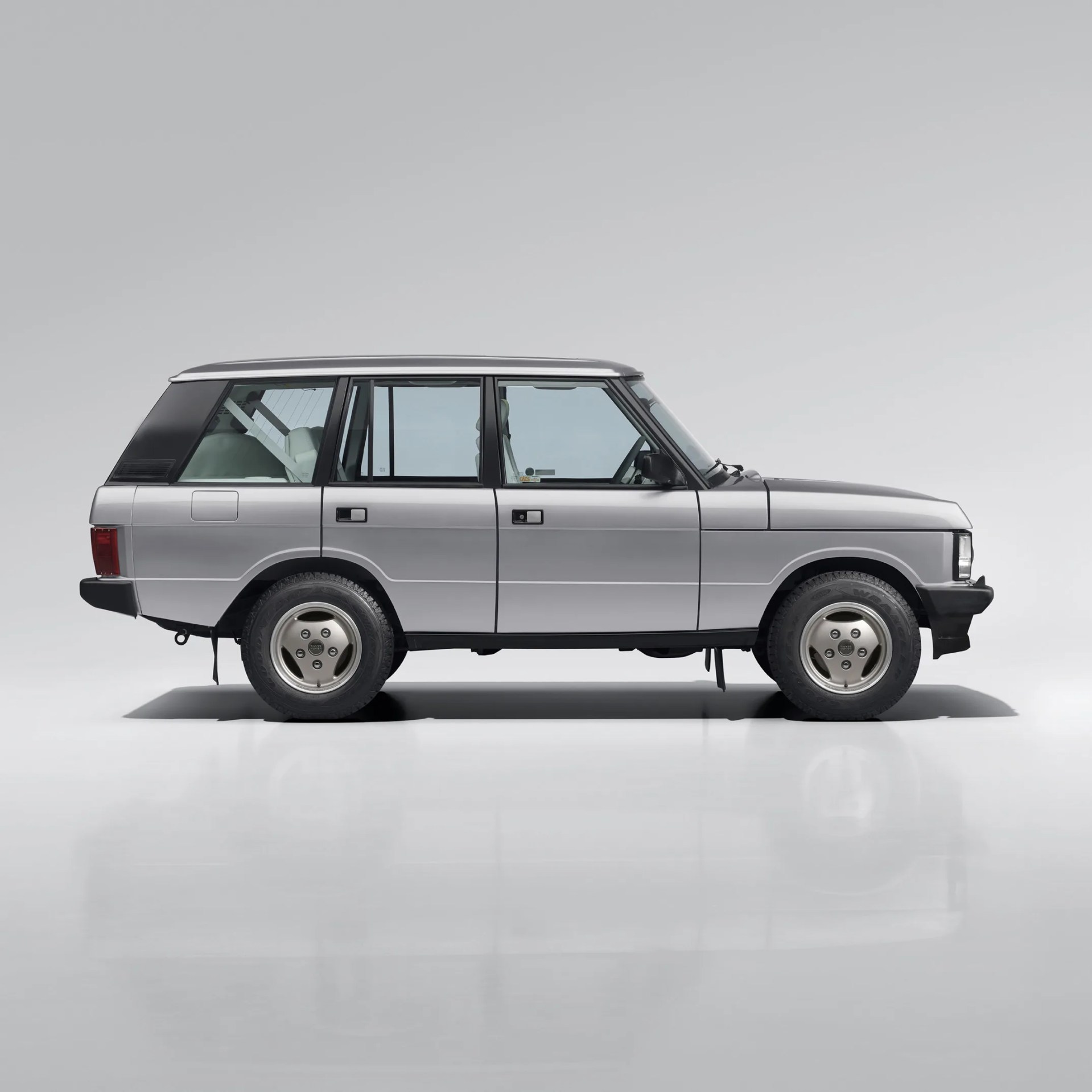 Silver classic Range Rover SUV side view with black trim and white interior seats visible through windows