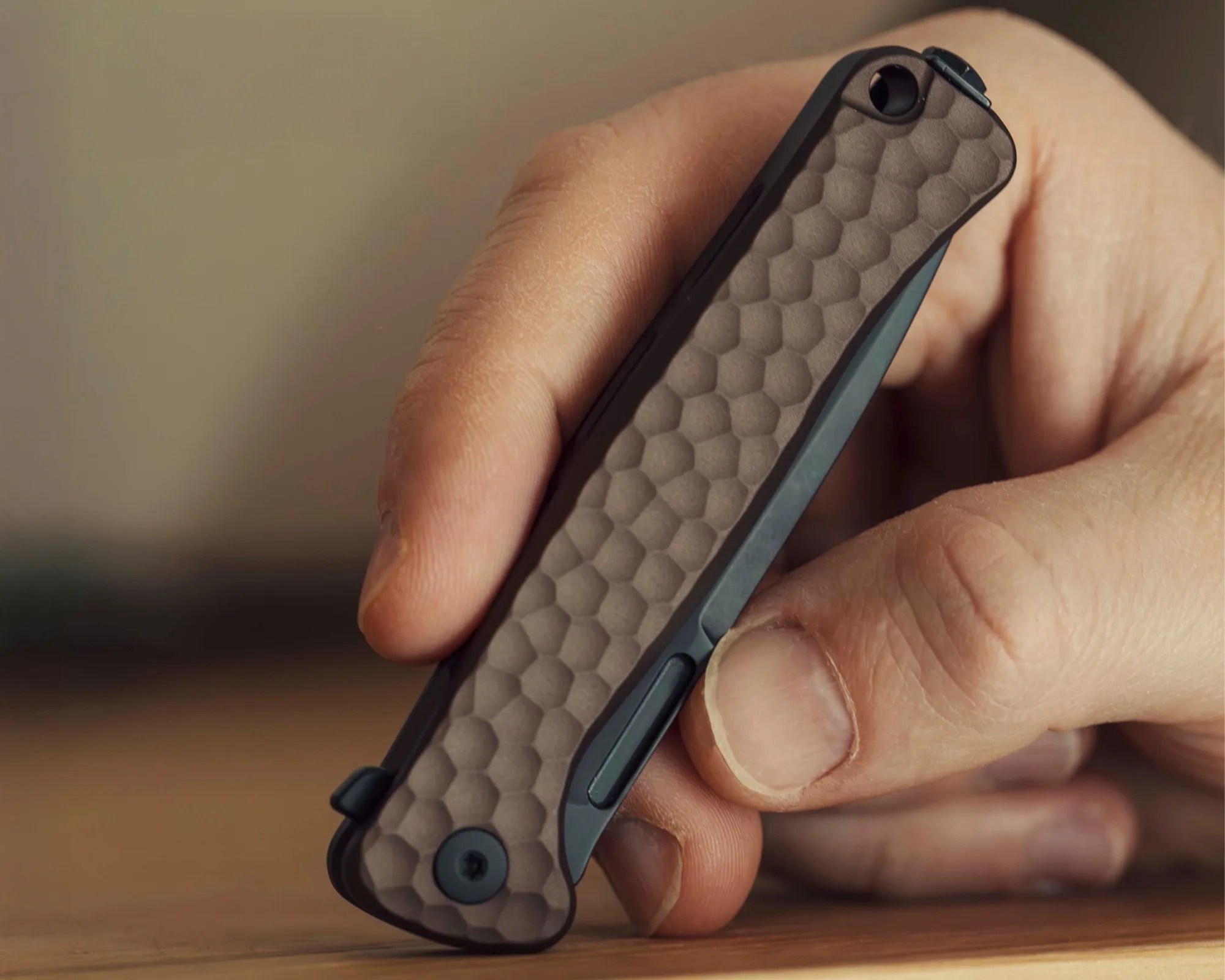 Hand holding a closed folding knife with a textured brown handle and black frame.