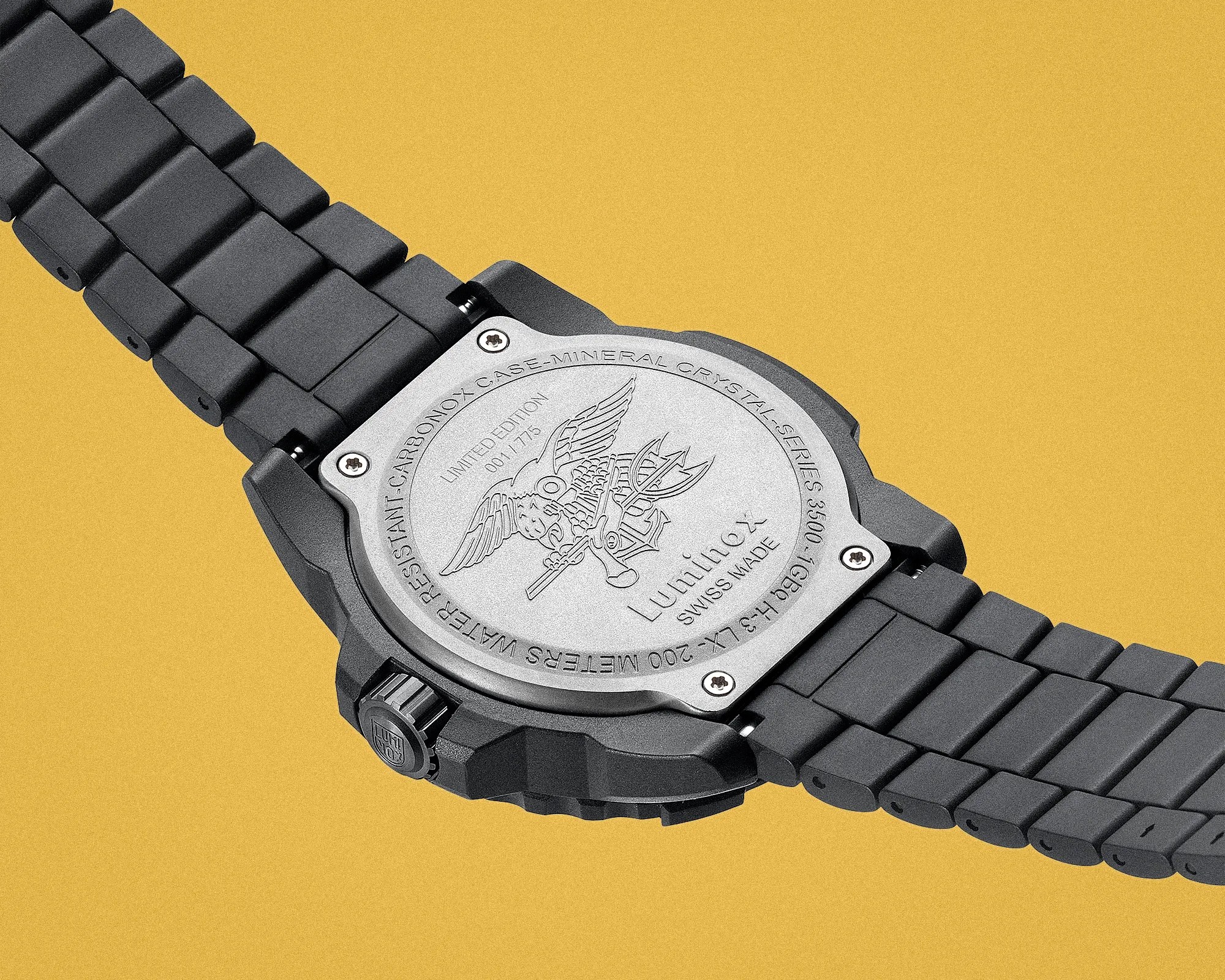 Close-up of the back of a black Luminox watch with a metal case back engraved with a winged emblem and text on a yellow background.