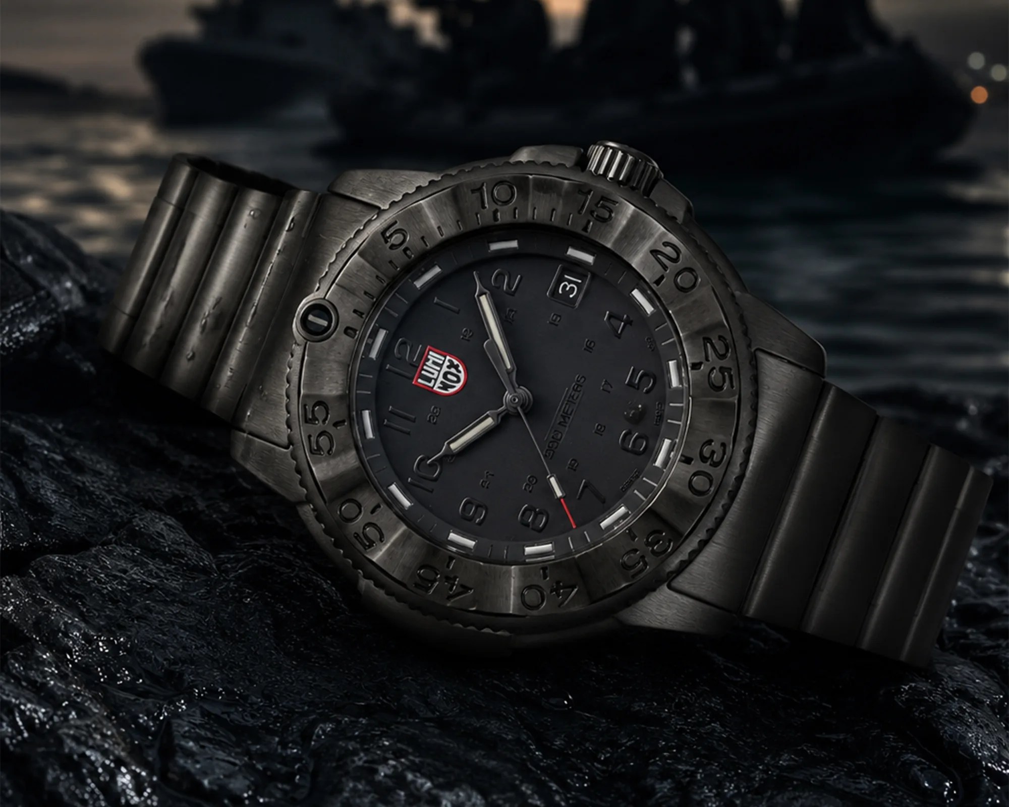 Black Luminox wristwatch with metal band on textured dark surface near water.