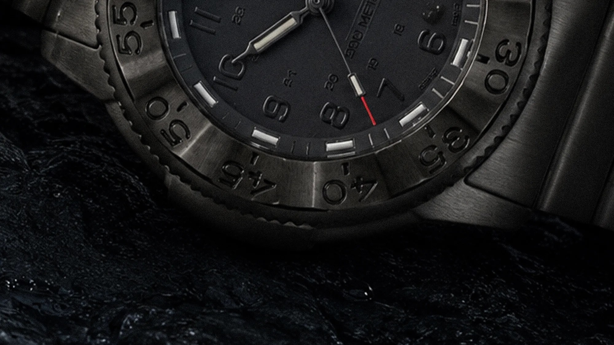 Close-up of a black metal wristwatch with a rotating bezel showing minute markers and luminous hands on a textured dark fabric.