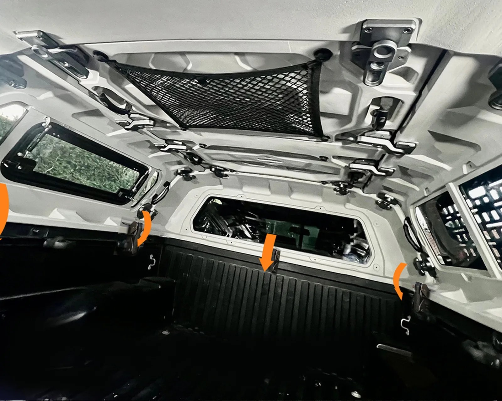Interior view of a vehicle's rear canopy with a black cargo net attached to the ceiling and multiple latches and handles.