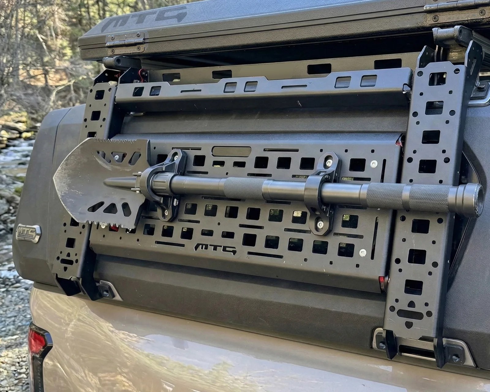 Black metal shovel mounted on a black MTC-branded rear vehicle rack.
