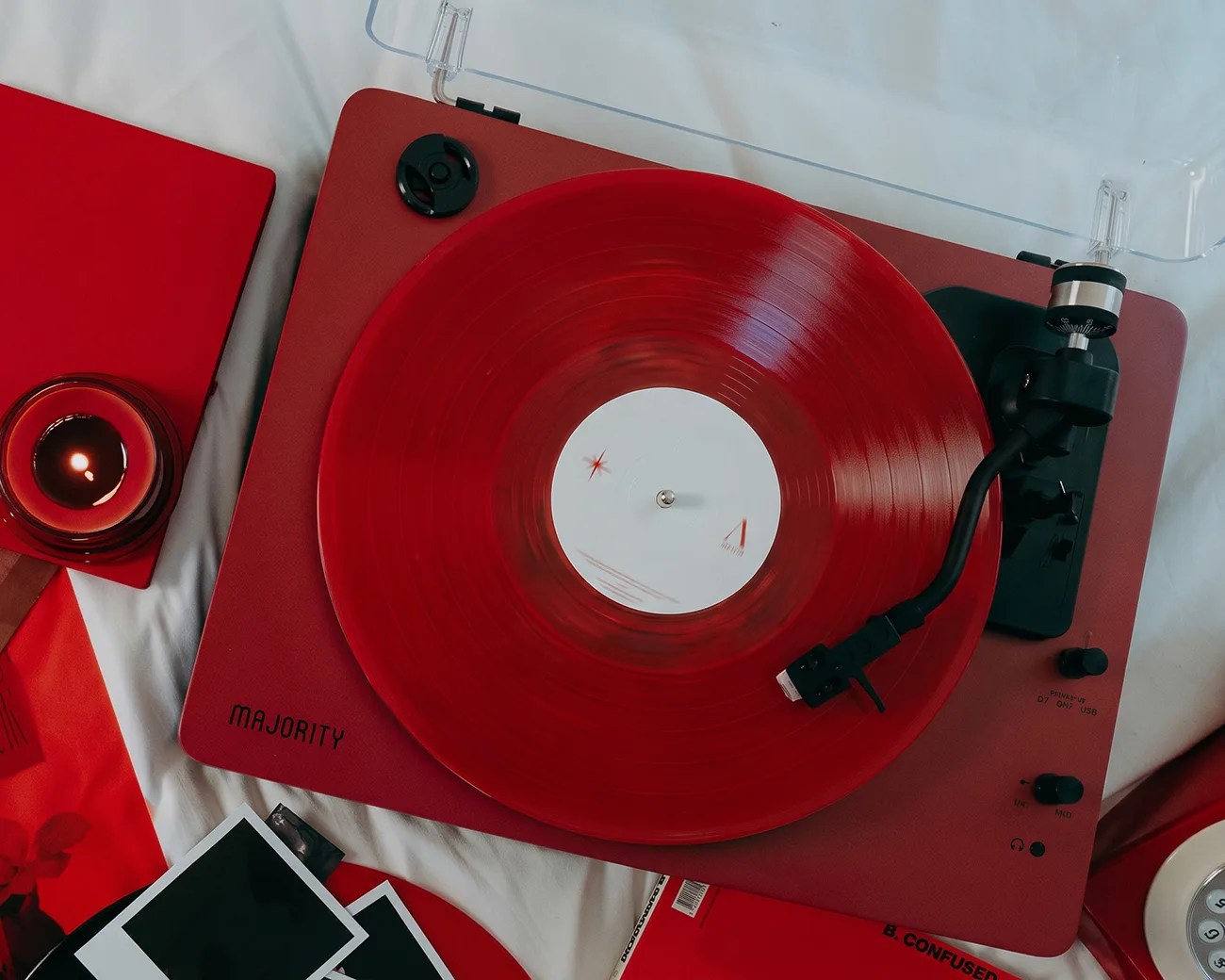 Red Majority brand turntable with a red vinyl record spinning, surrounded by red and white items on a white surface.