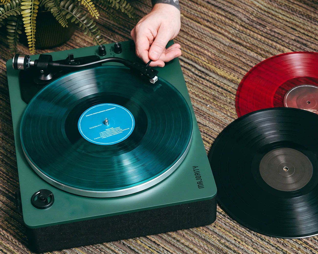 Green Majorty turntable playing a vinyl record with two additional vinyl records on a striped carpet.