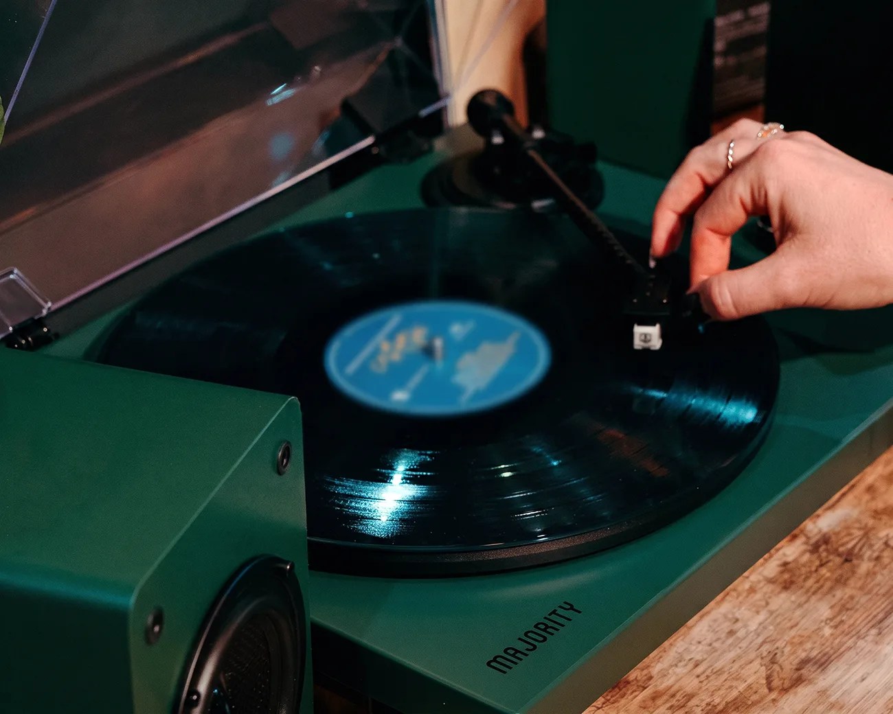 Green Majority turntable playing a vinyl record with a hand adjusting the tonearm.