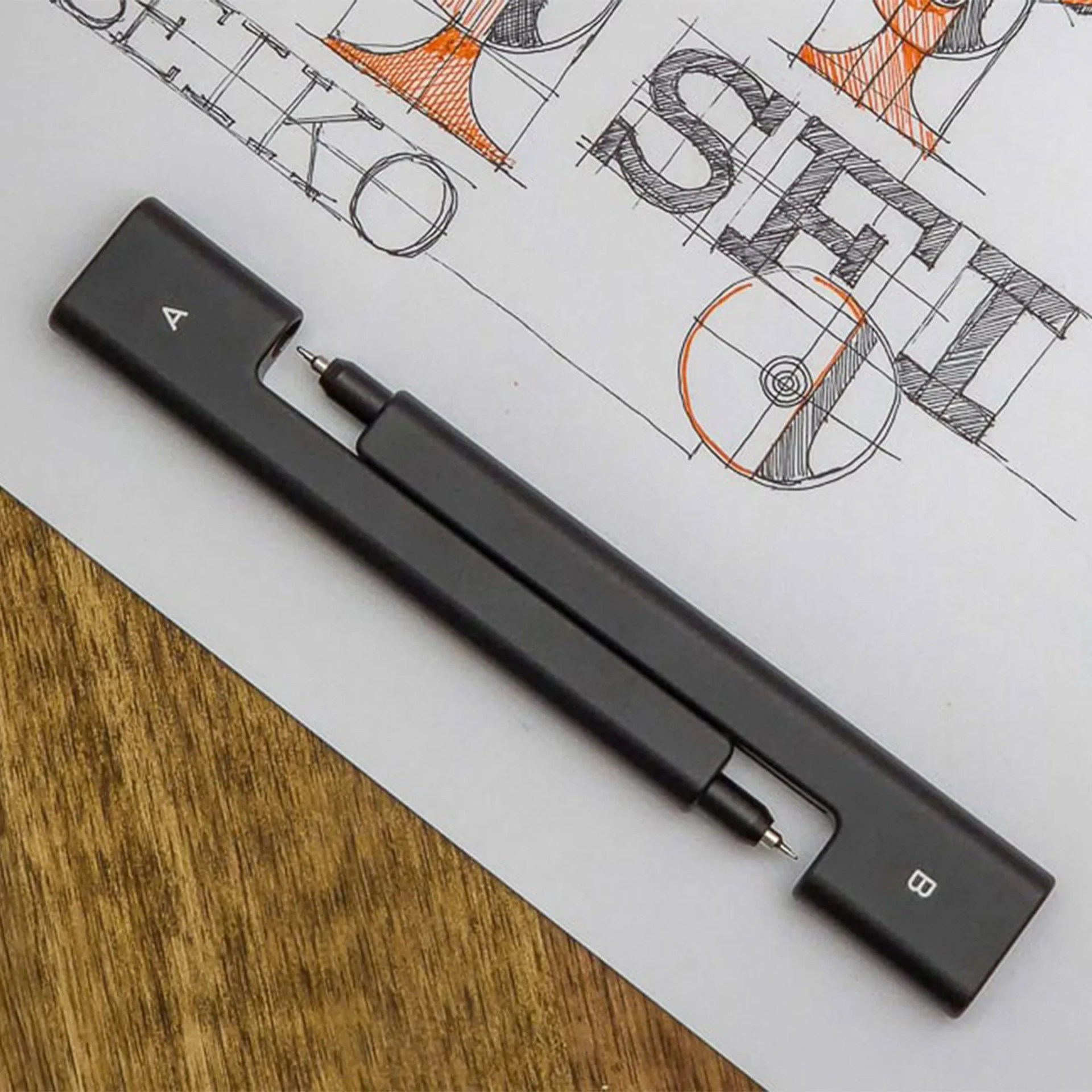 Black pen with a rectangular case labeled "A" and "B" resting on a paper with hand-drawn typography sketches.