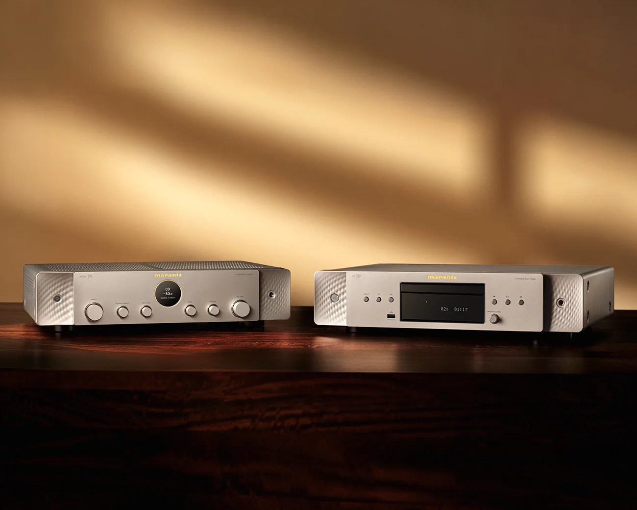 Two silver Marantz audio components, an amplifier and a compact disc player, on a wooden surface with warm lighting.