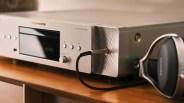 Silver Marantz compact disc player with black headphones plugged in, placed on a wooden surface.