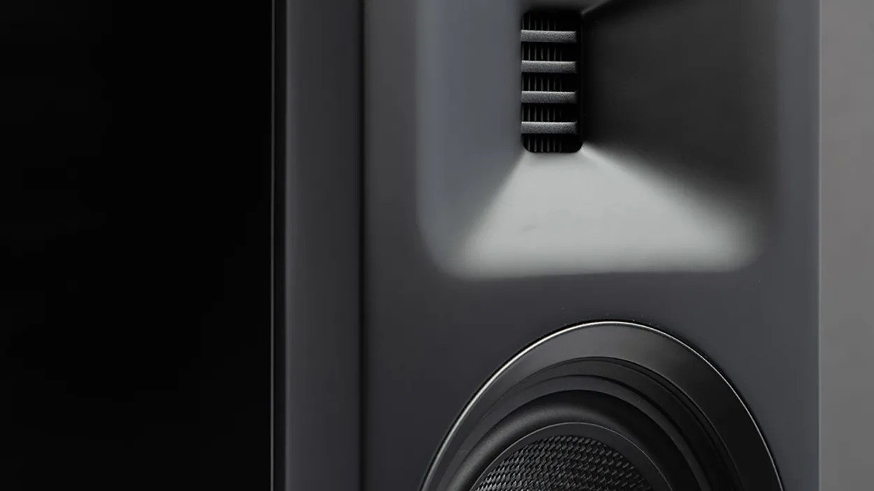 Close-up of a black speaker with a textured woofer and a rectangular tweeter on a matte black surface.