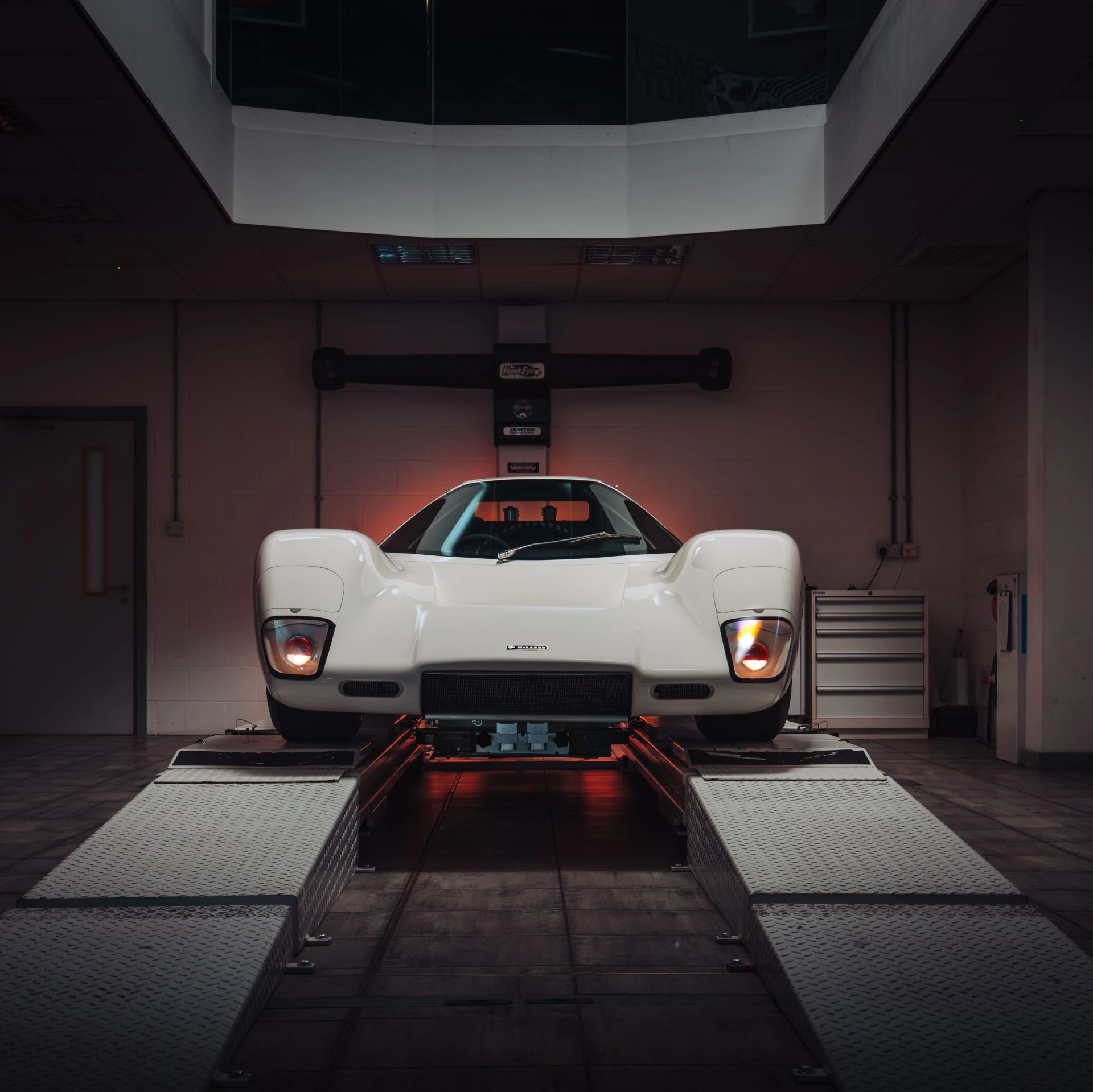 White vintage sports car with pop-up headlights on a car lift inside a garage.