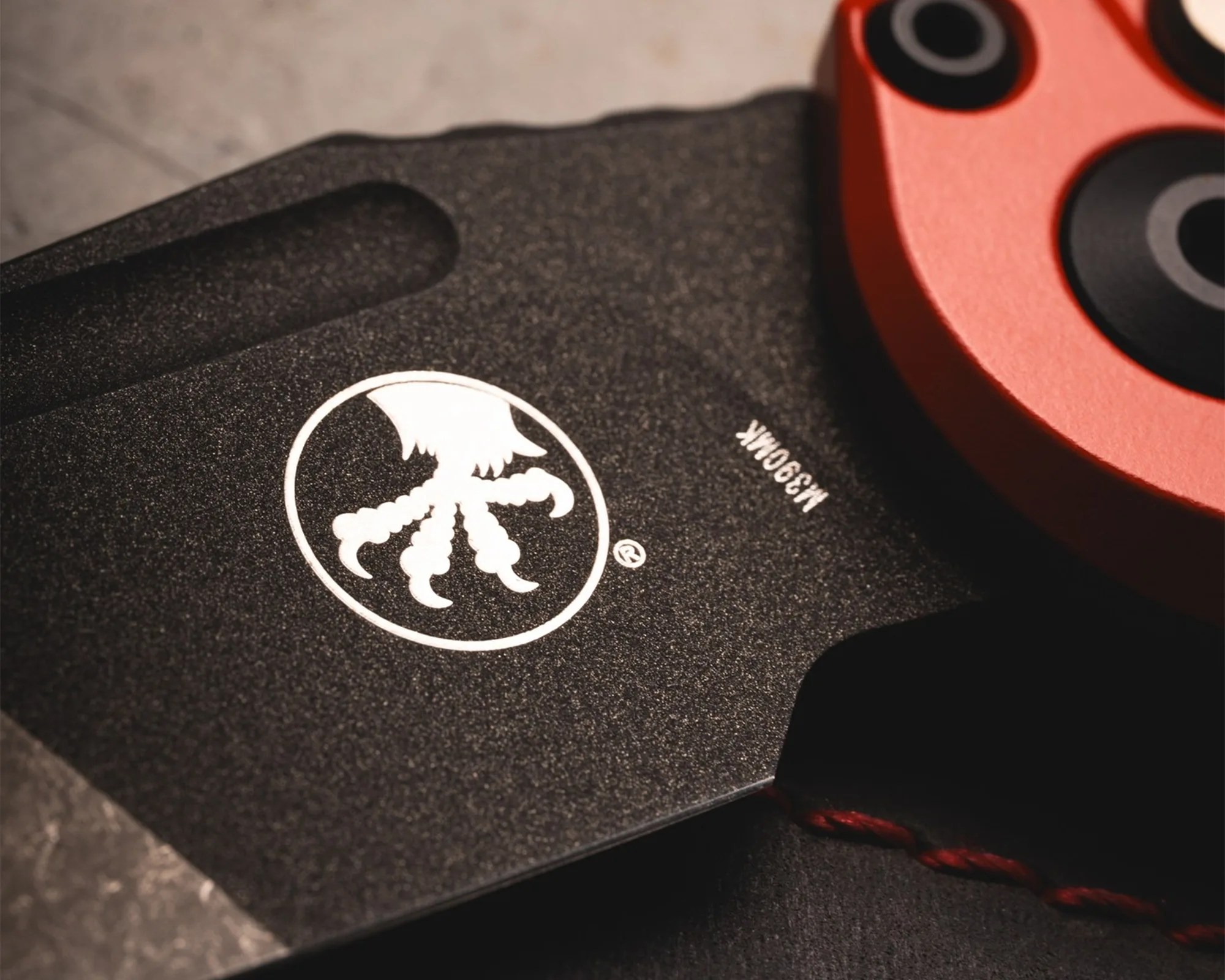 Close-up of a black textured knife blade with a white octopus logo and red handle.