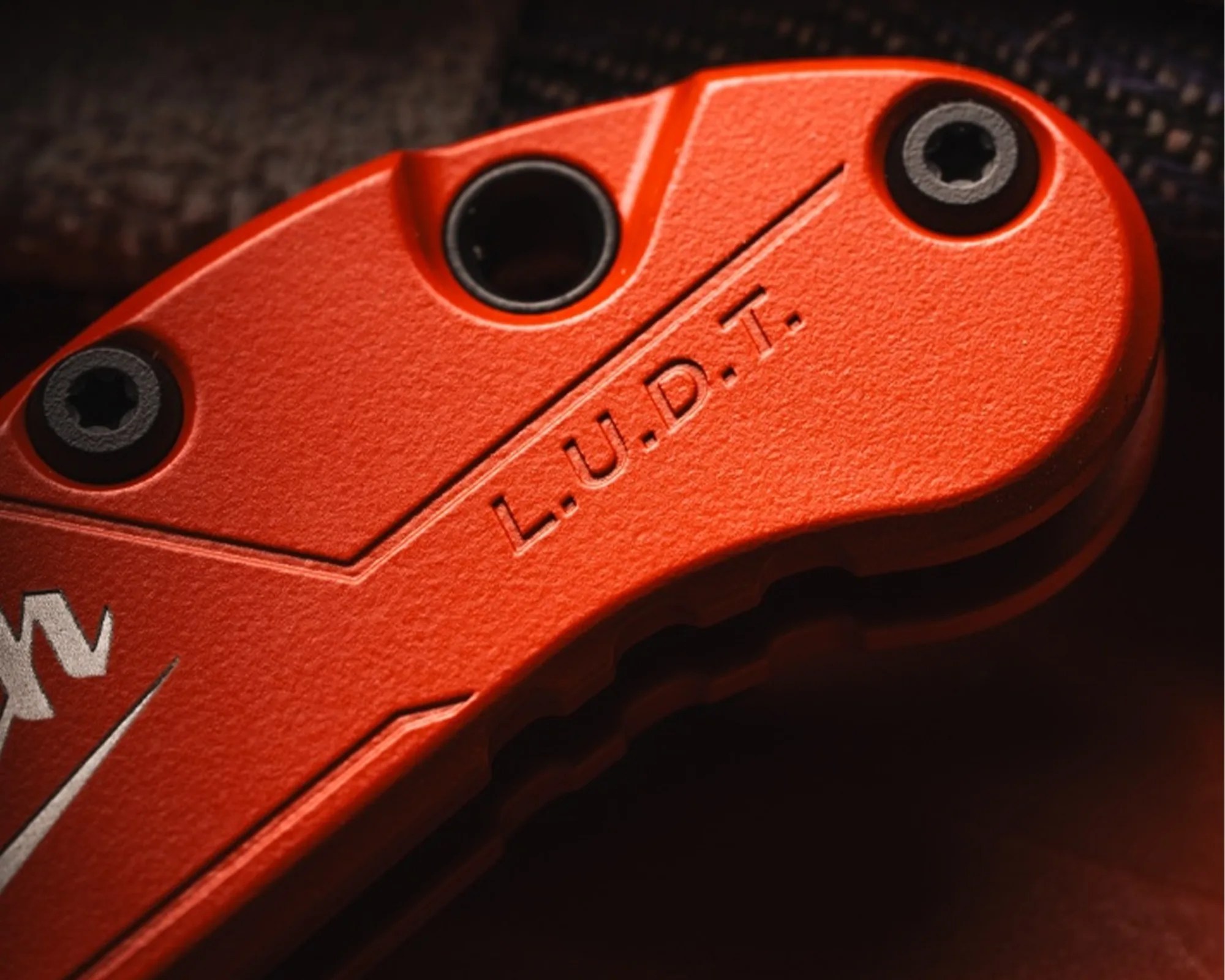 Close-up of an orange textured tool handle with black screws and engraved text "L.U.D.T.