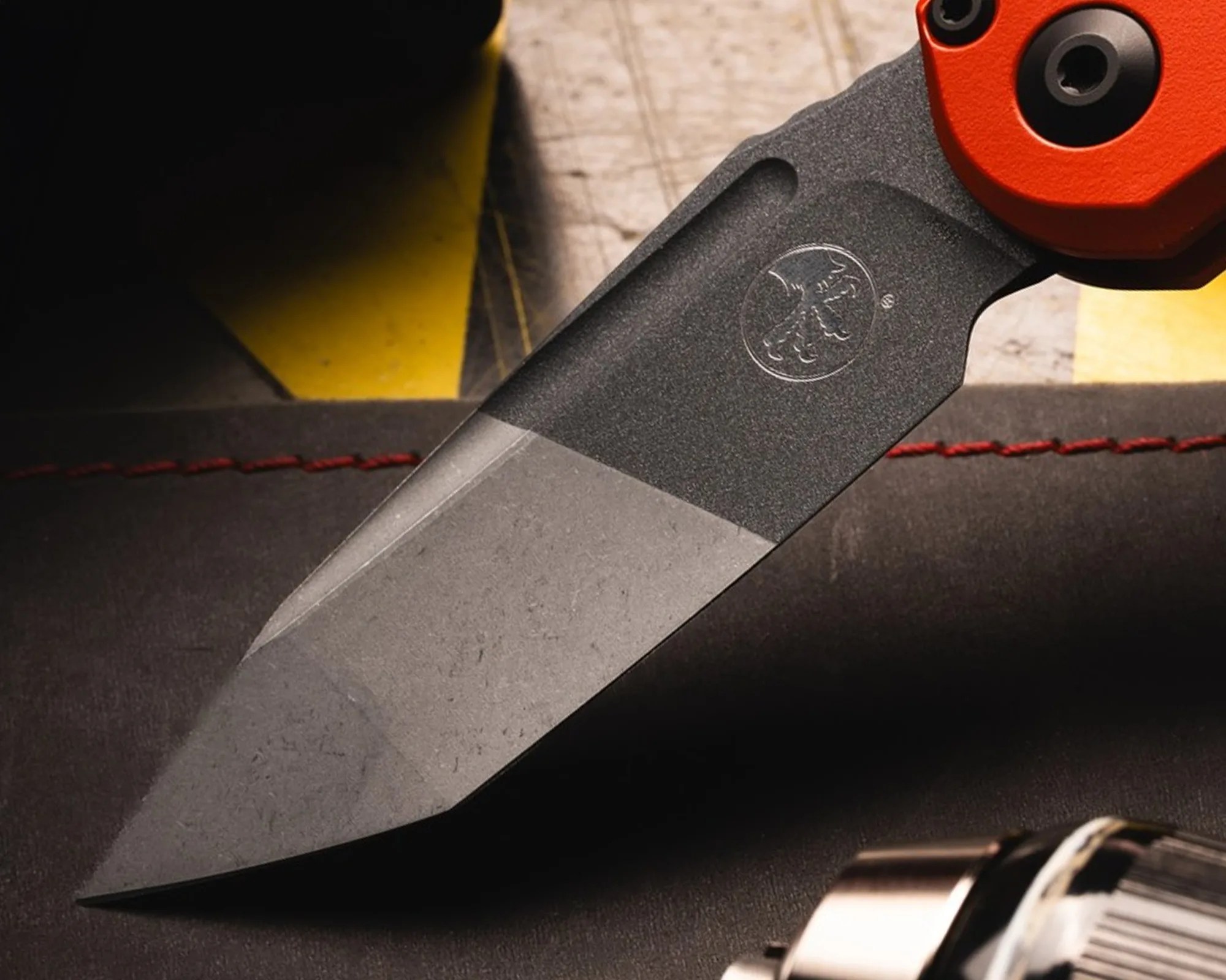 Close-up of a two-tone gray knife blade with a textured black section and an orange handle.