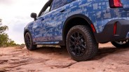 Blue SUV with digital camouflage pattern and black off-road tires on rocky terrain.