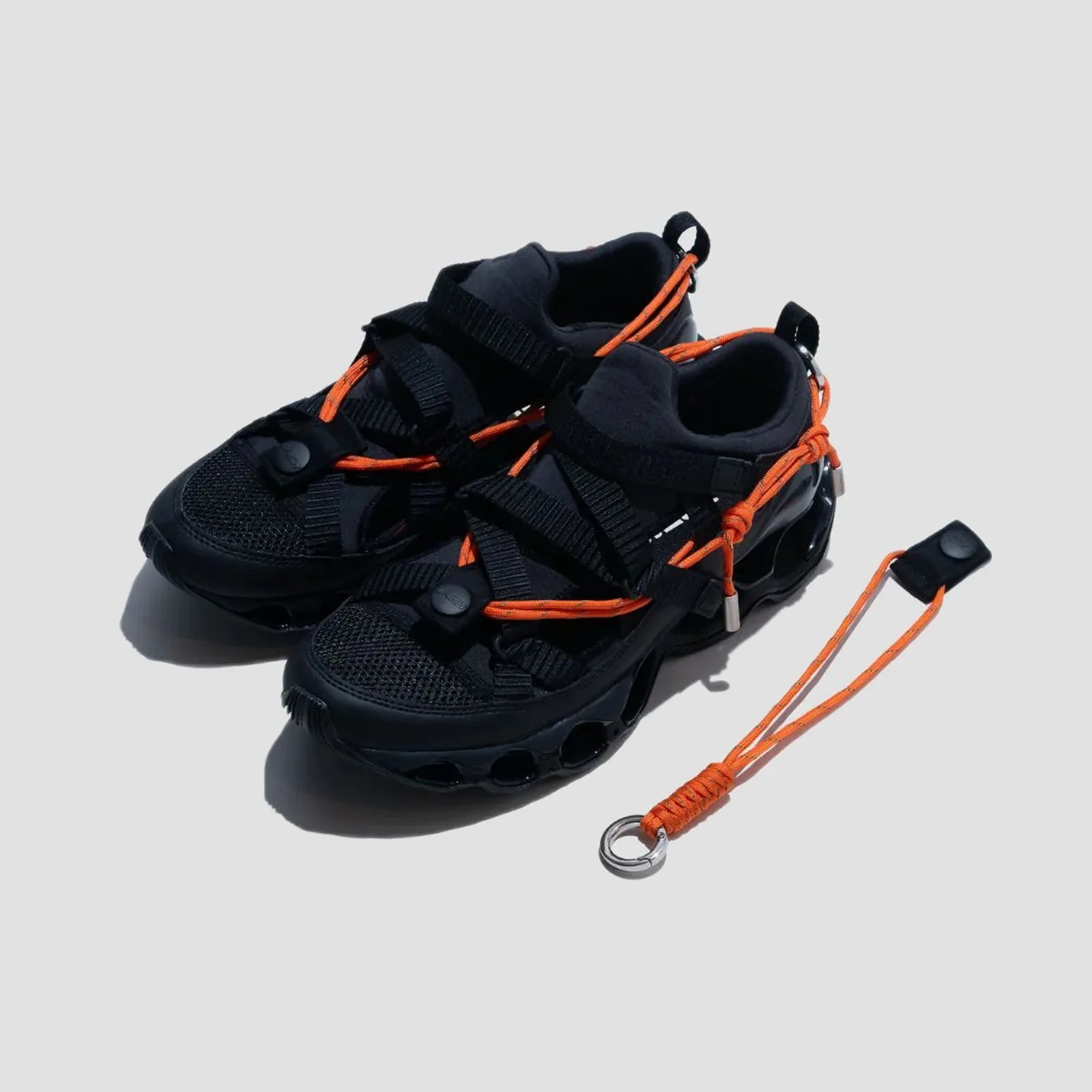 Pair of black athletic shoes with orange laces and a matching orange keychain on a light gray background.