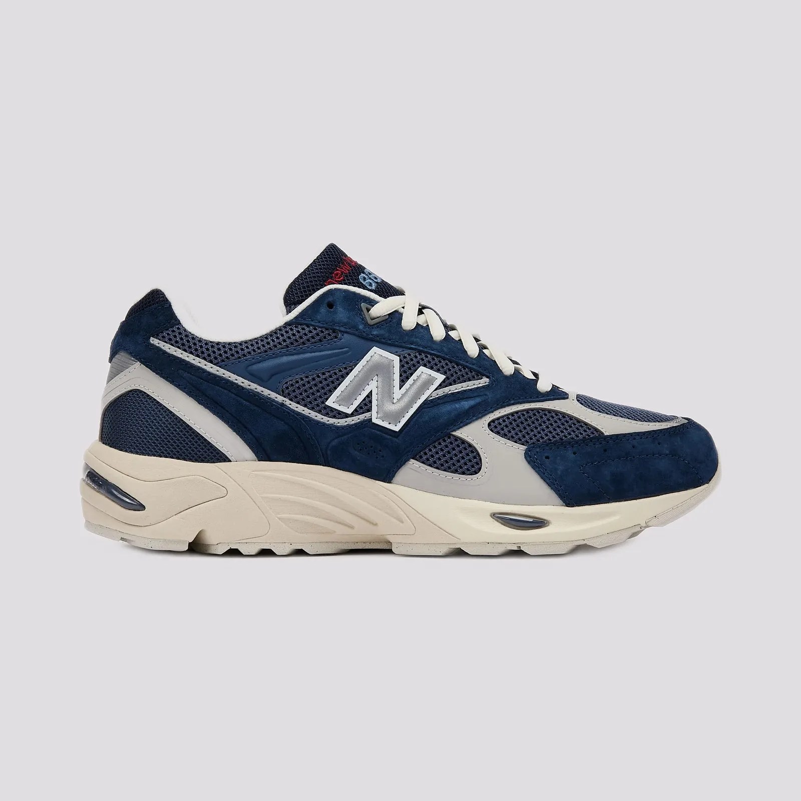 Navy blue and gray New Balance sneaker with white laces and beige sole on a gray background.