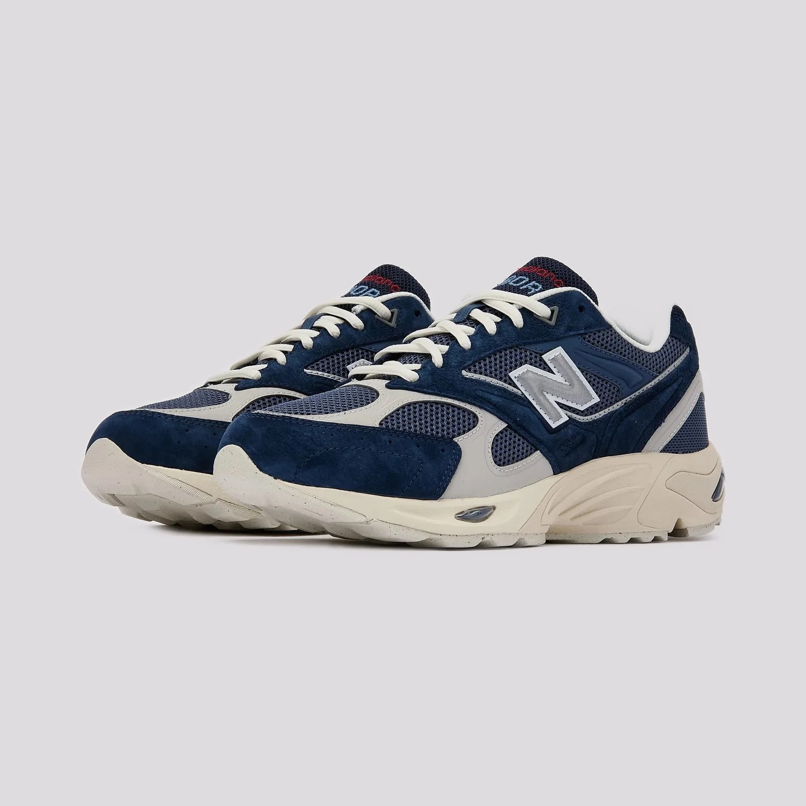 Pair of navy blue and gray New Balance sneakers with white laces and beige soles on a gray background.