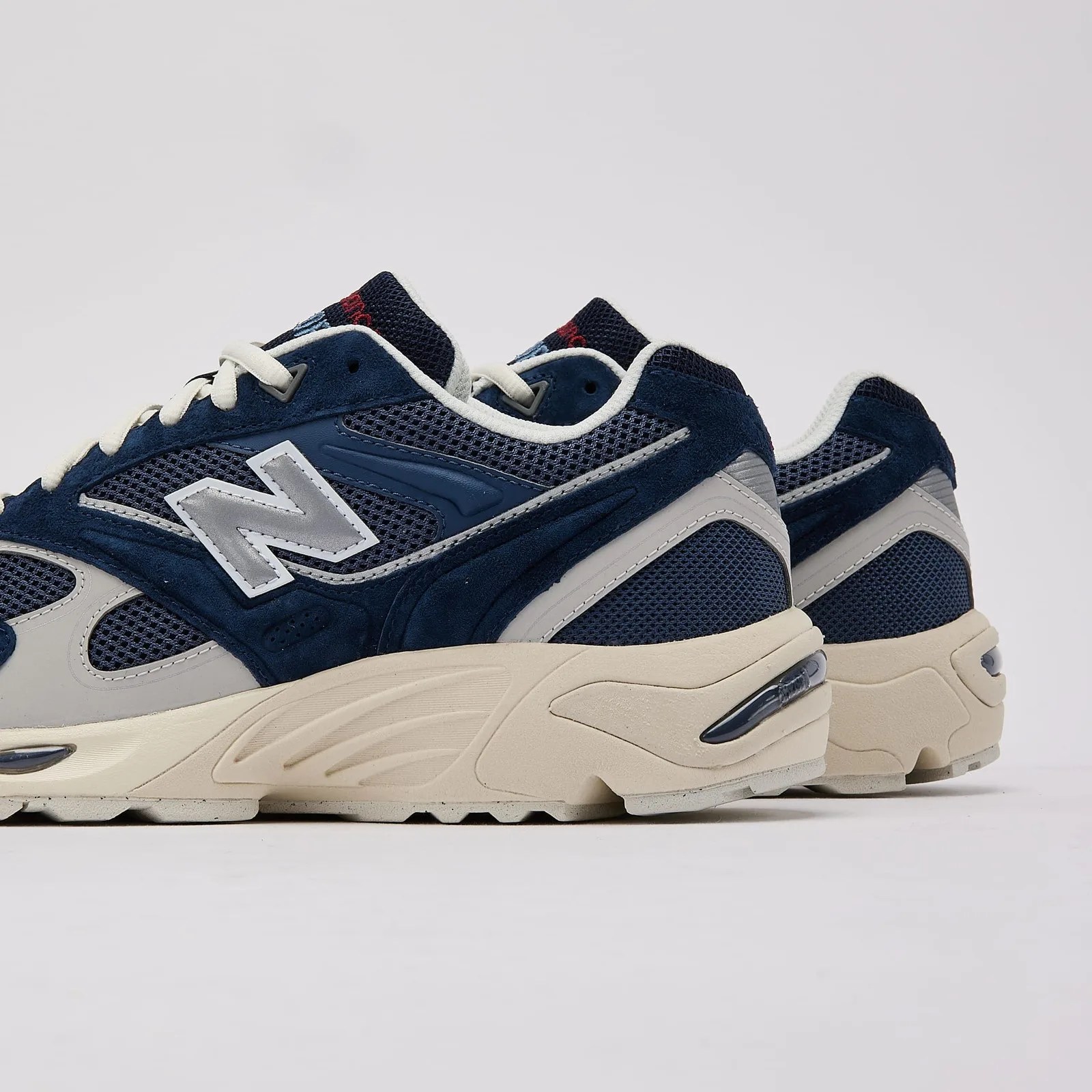 Pair of navy blue and gray New Balance sneakers with white laces and beige soles on a white background.
