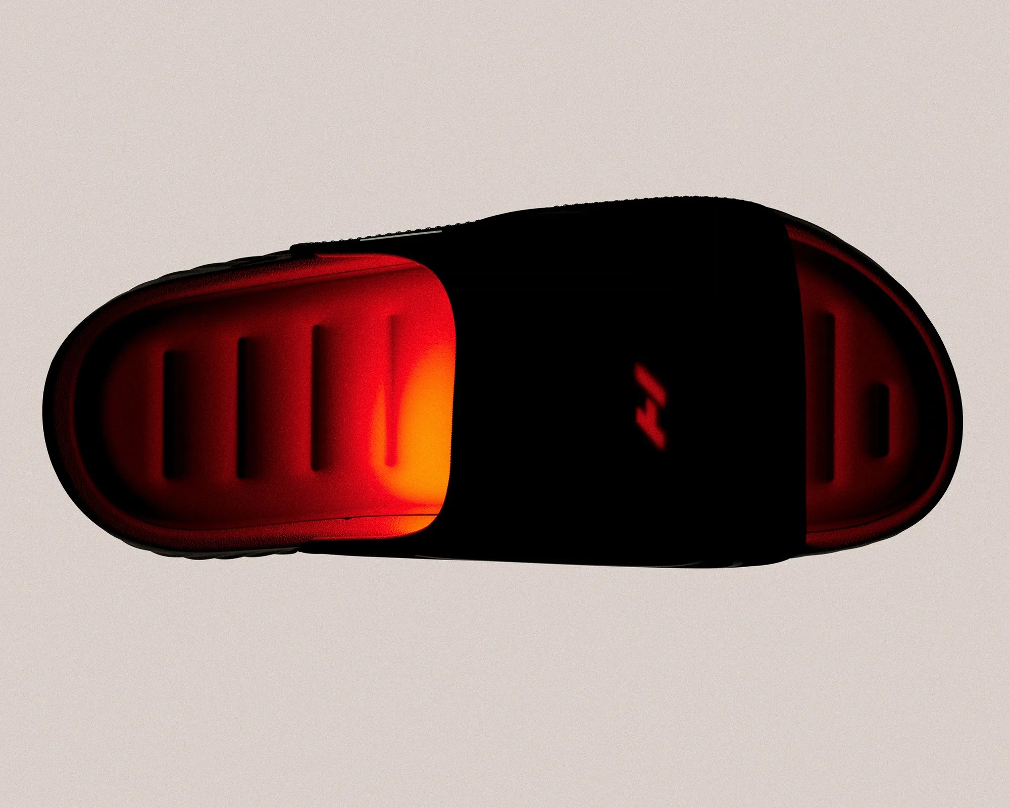 Black slide sandal with a bright red cushioned footbed on a beige background.