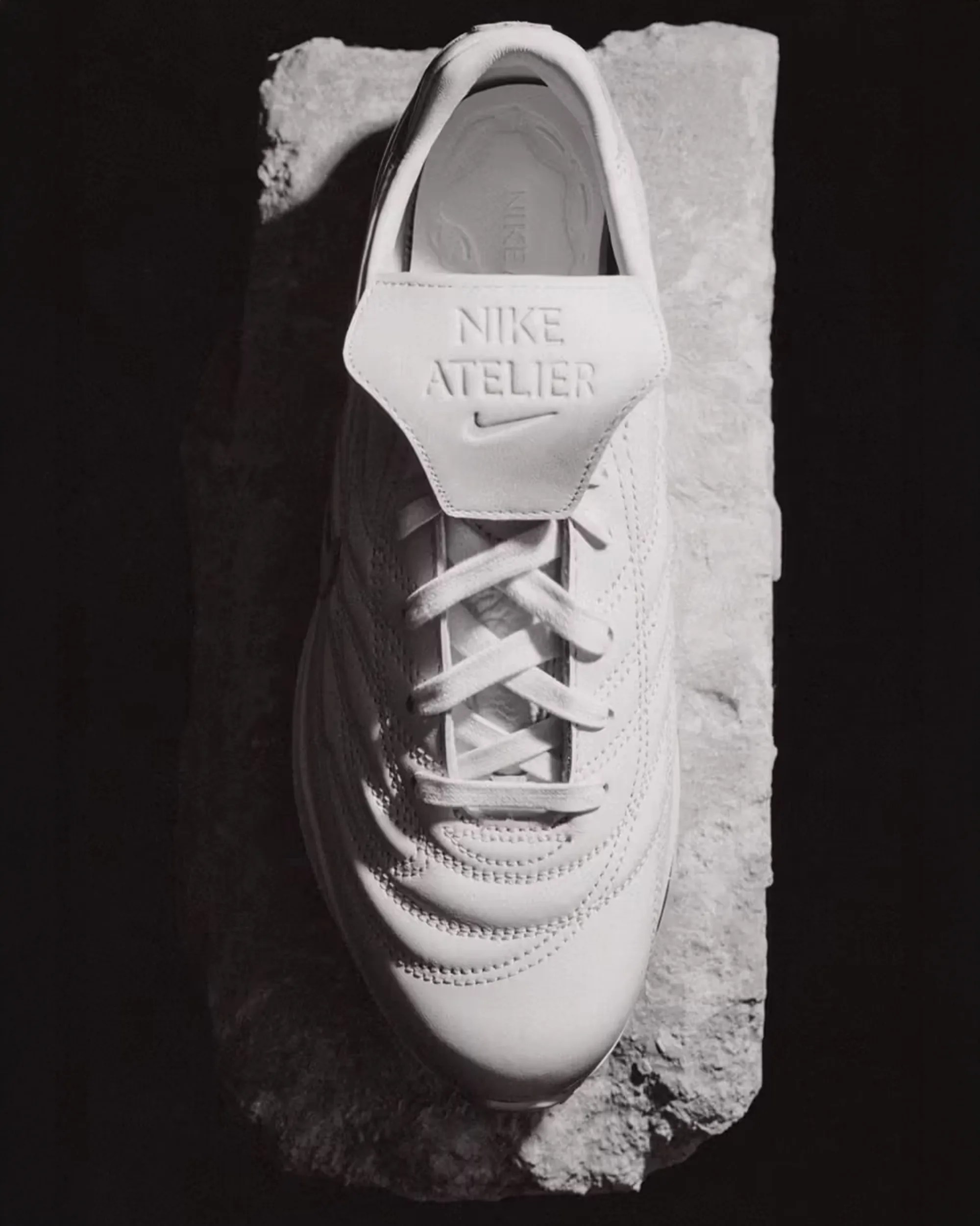 White Nike Atelier sneaker with laces on a rough stone slab against a dark background.