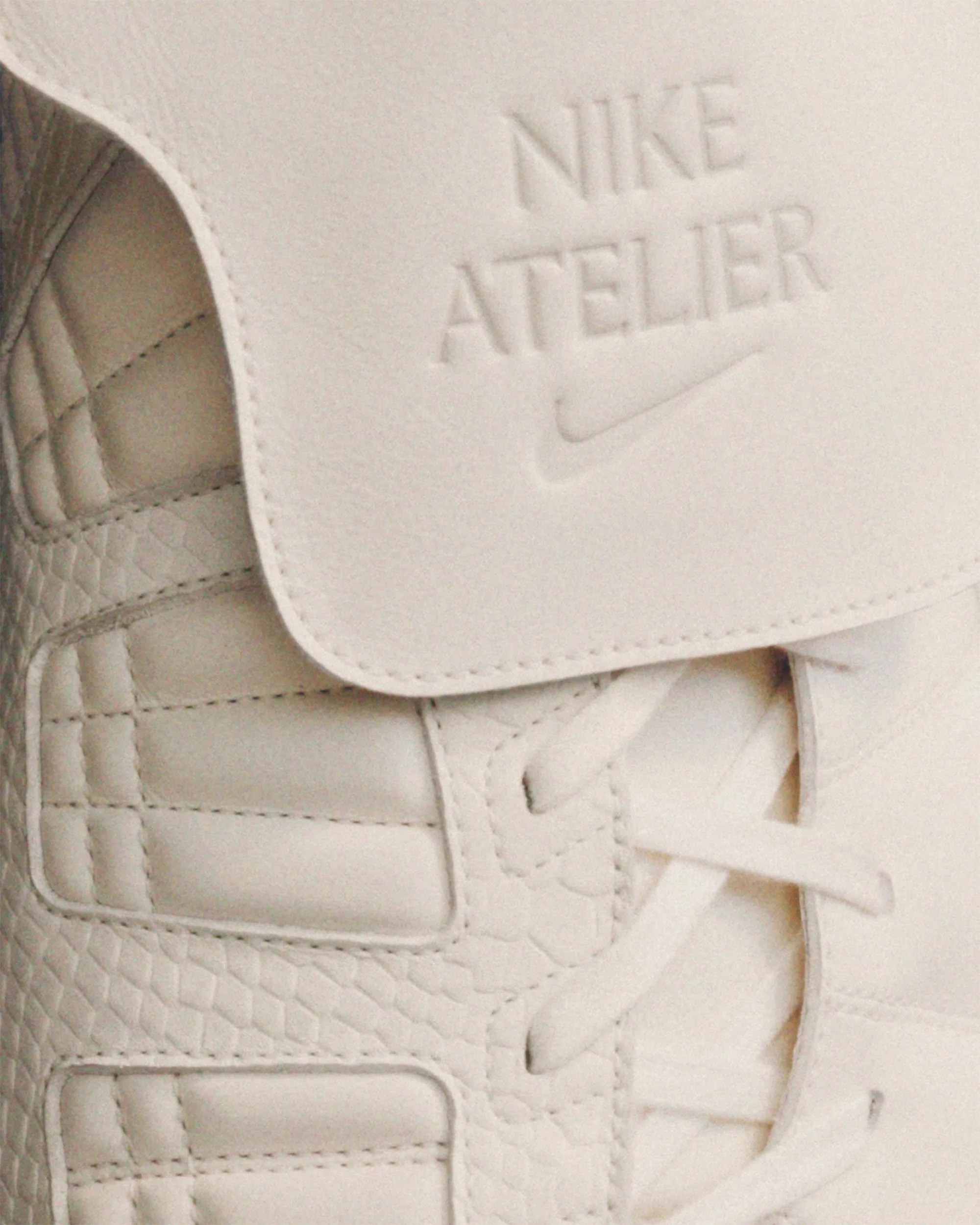 Close-up of a beige Nike Atelier sneaker showing textured leather, laces, and embossed logo on the tongue.