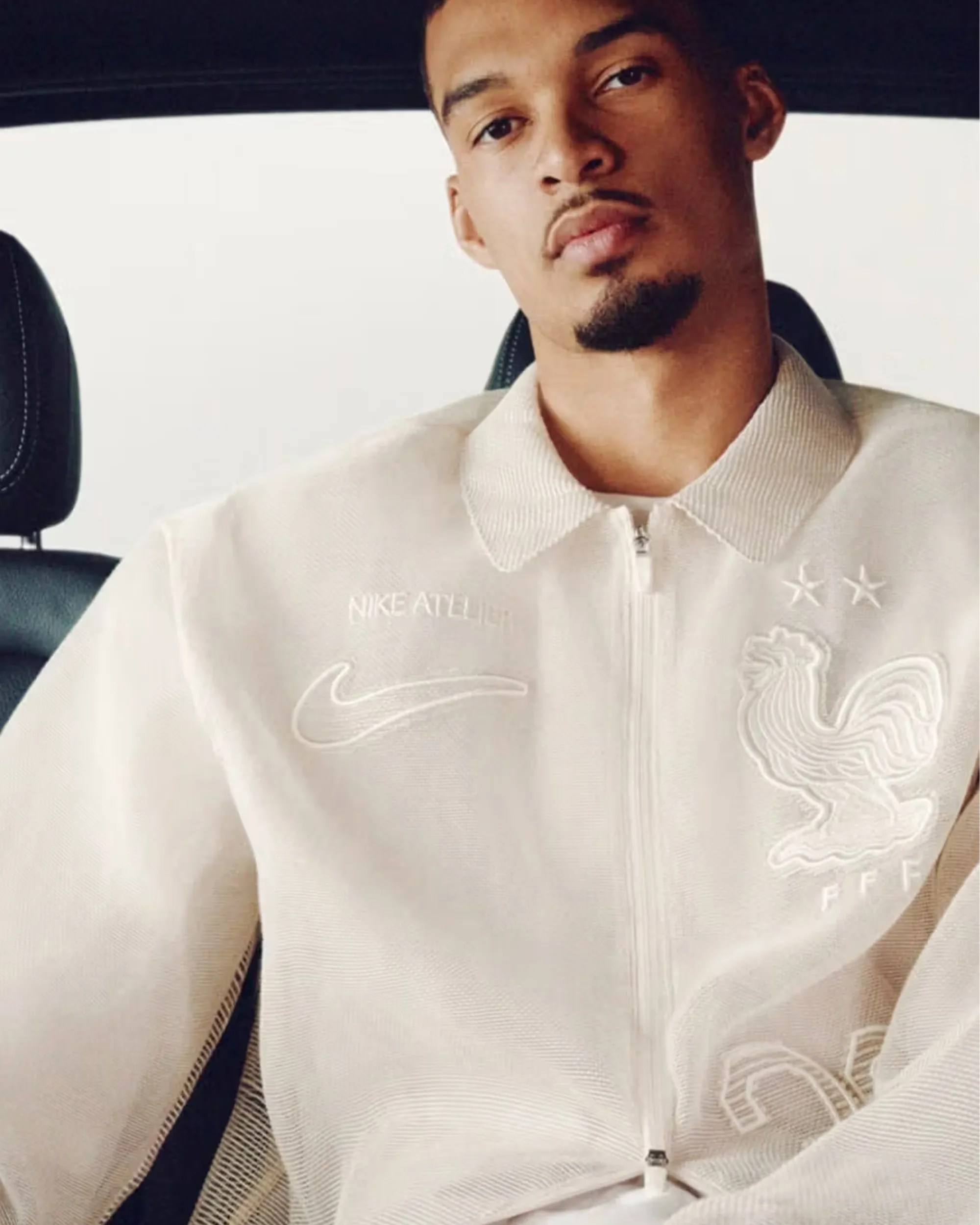 Beige zip-up jacket with Nike swoosh, "NIKE ATHLET" text, and rooster emblem with two stars on chest.