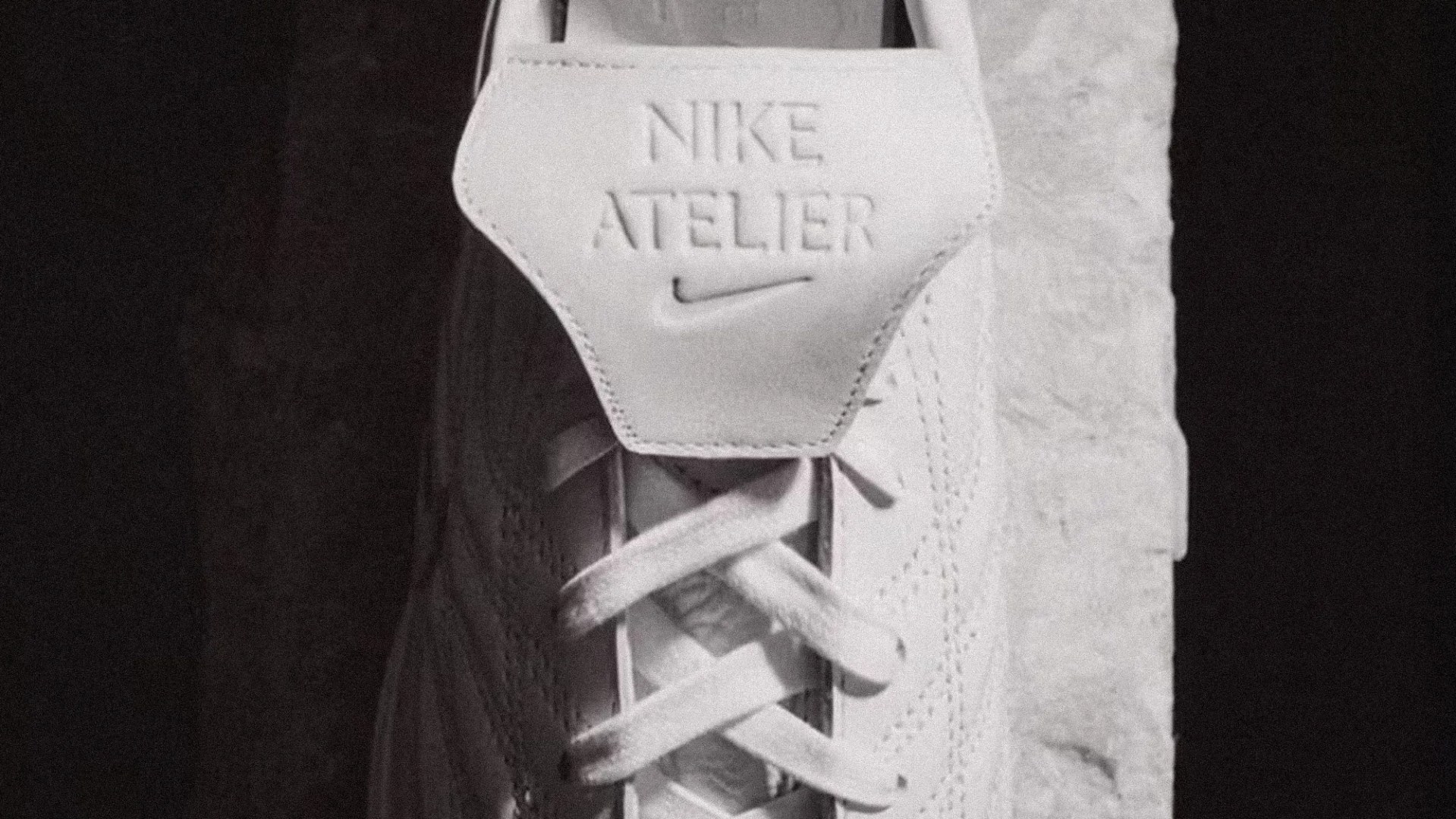 Close-up of white Nike Atelier sneaker tongue with embossed logo and laces.