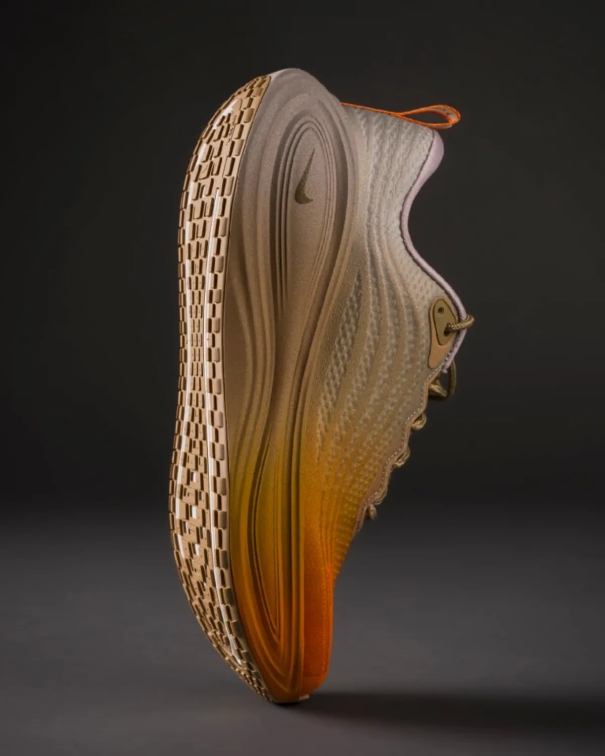 Side view of a beige and orange Nike sneaker with textured sole and pull tab on a dark background.