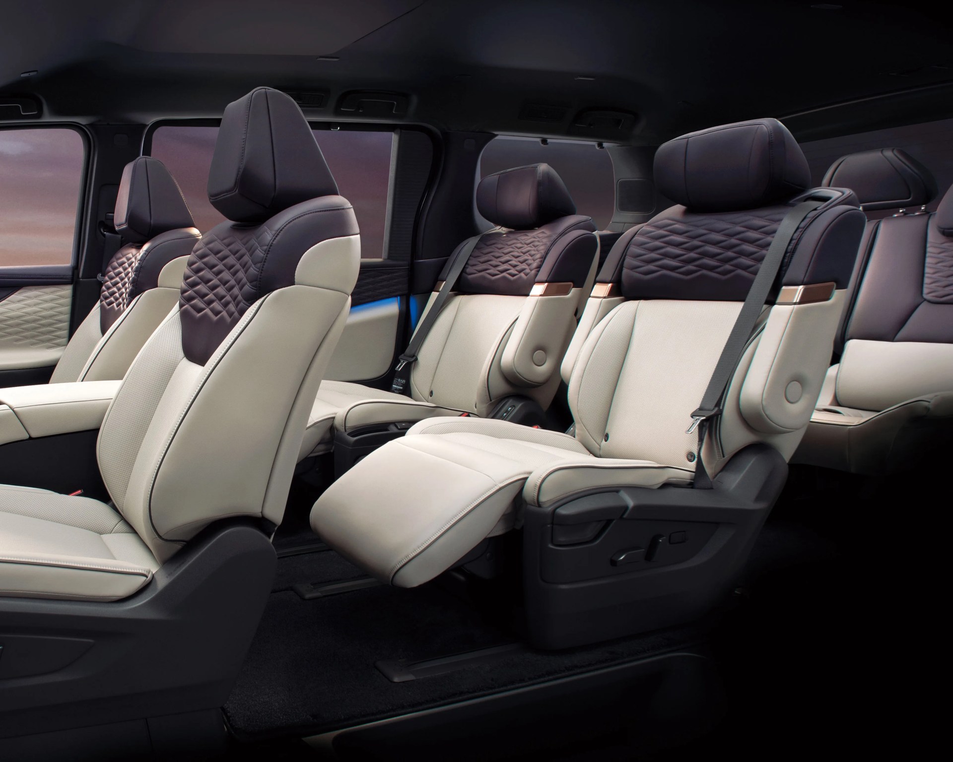 Four beige and dark brown leather car seats with quilted headrests and one seat reclined with extended leg rest.