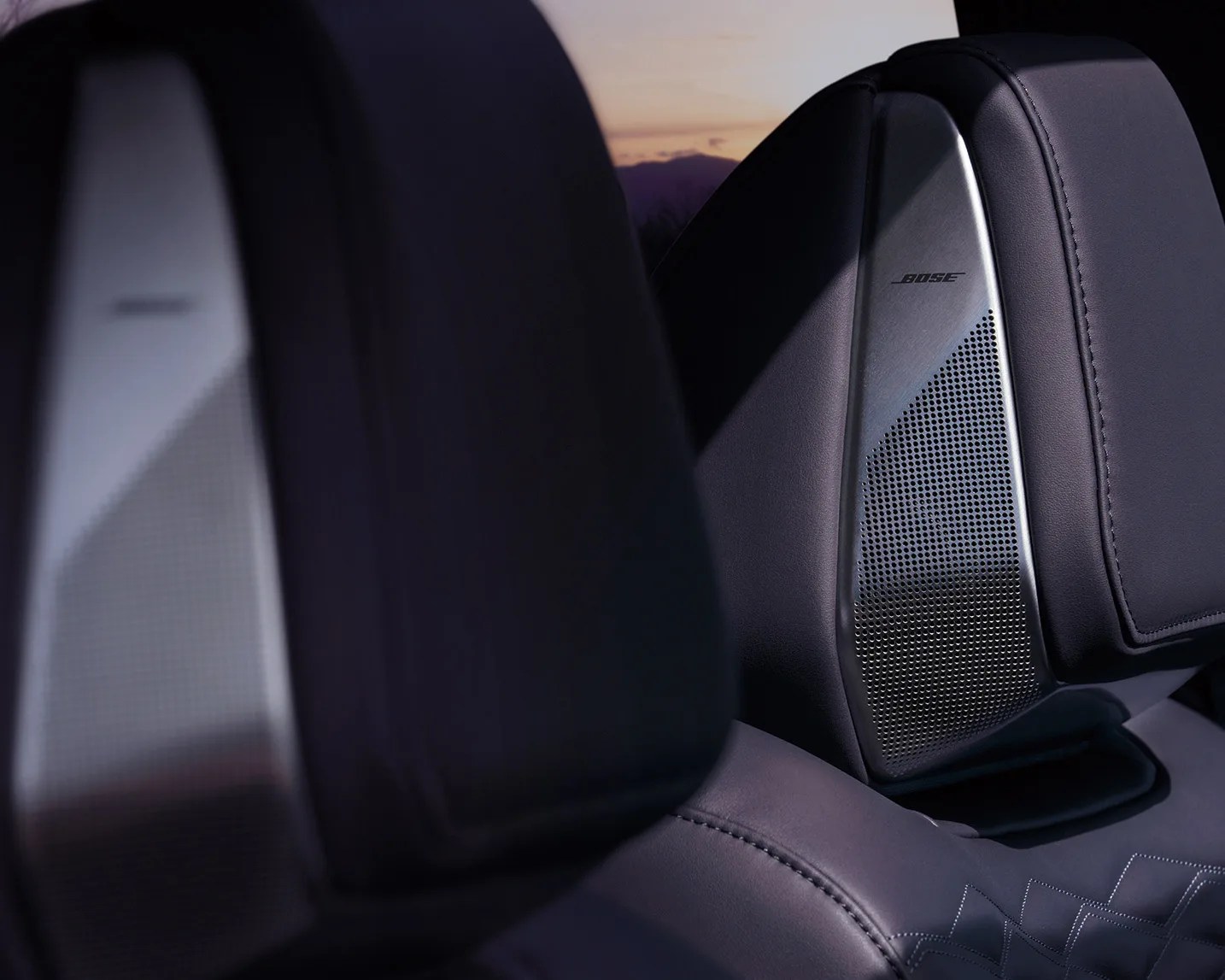 Close-up of black leather car seats with integrated silver Bose speakers in the headrests.