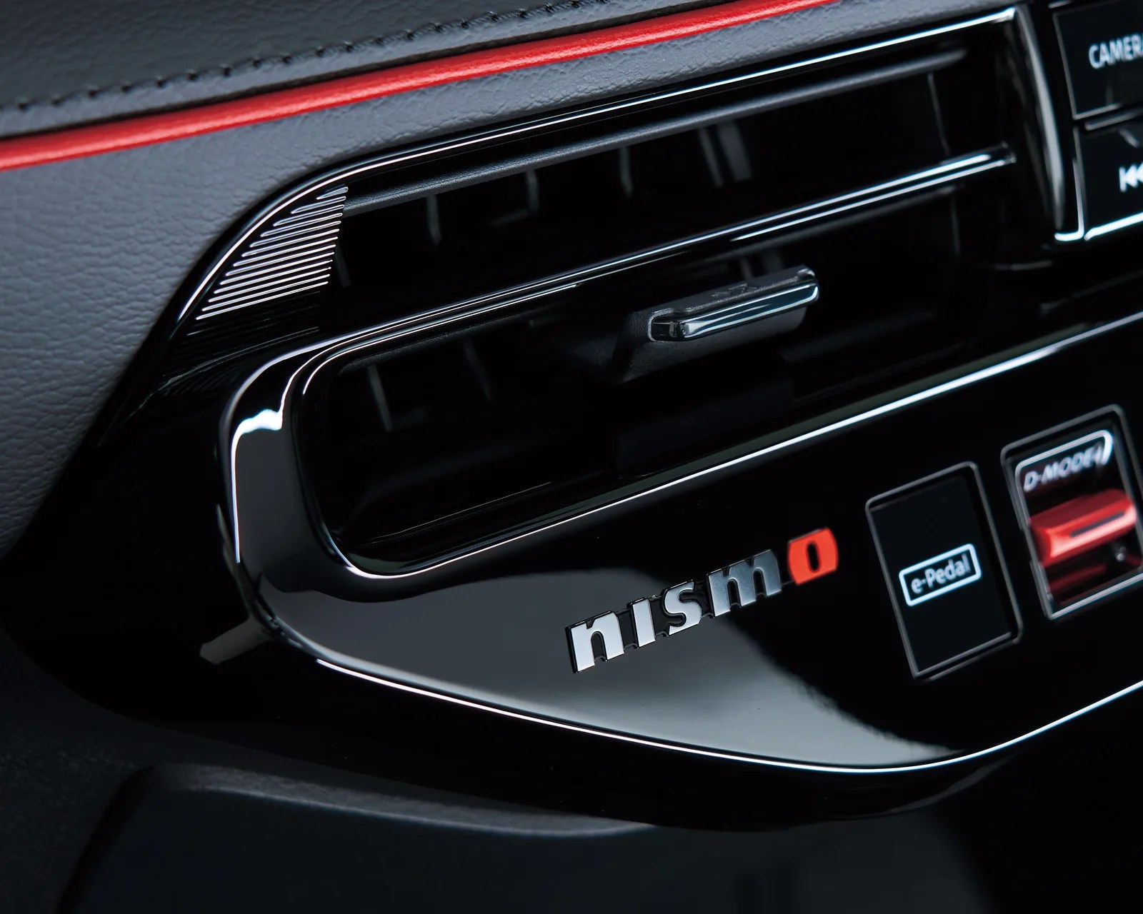 Glossy black car dashboard panel with "nismo" logo, air vent, and buttons labeled "e-Pedal" and "D-MODE.