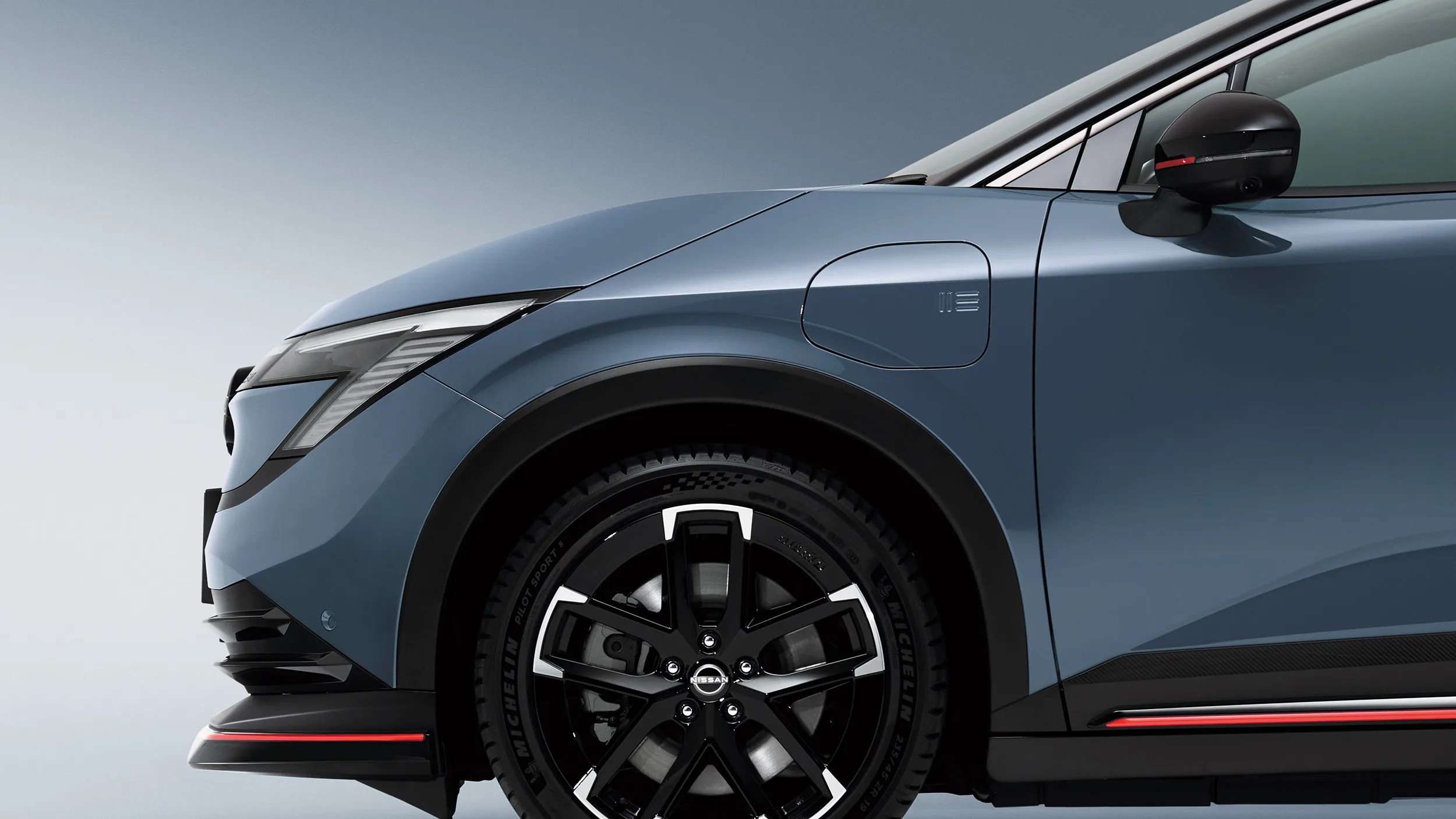 Close-up of a blue electric car's front left side showing the wheel, charging port, and side mirror.