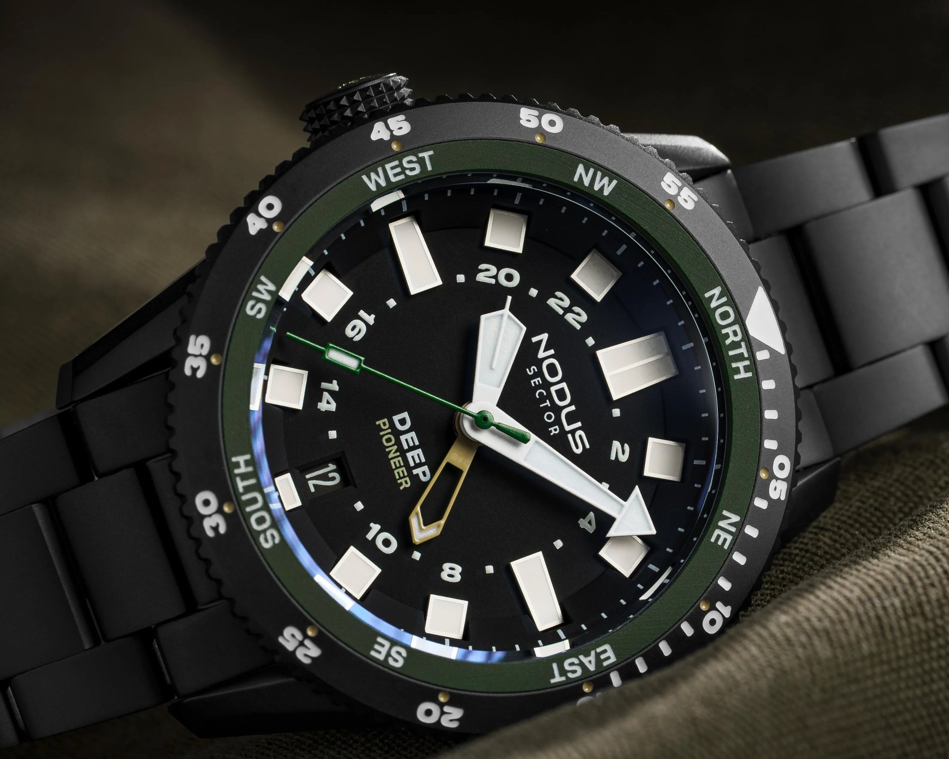Black wristwatch with white rectangular hour markers and green bezel showing compass directions.