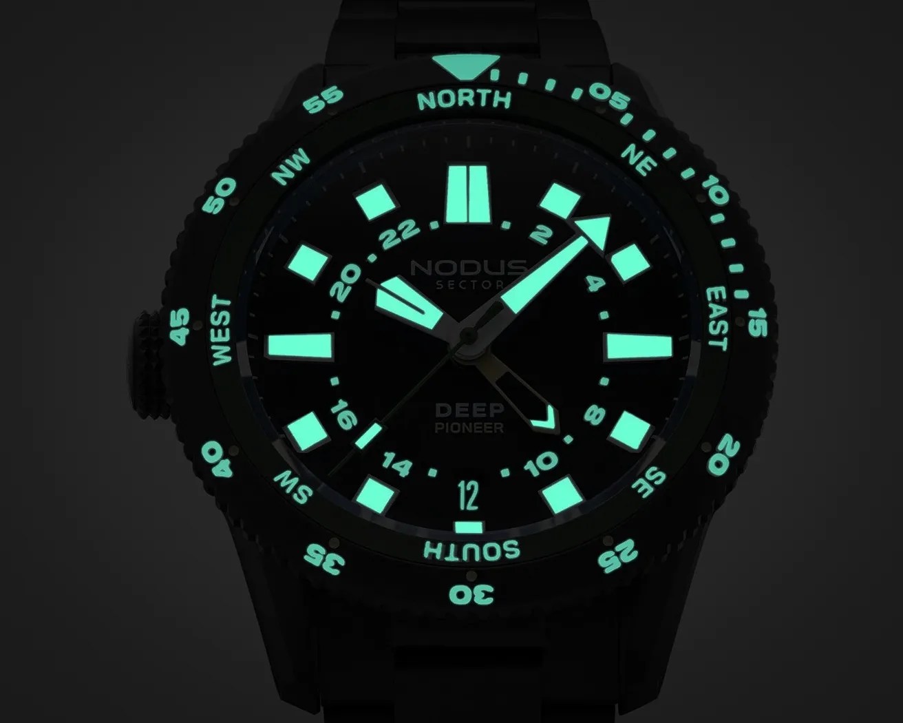 Black dive watch with glowing turquoise hour markers, hands, and compass bezel markings in a dark setting.