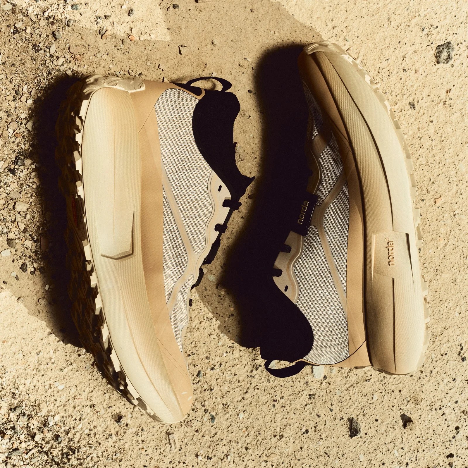 Pair of beige and black trail running shoes with textured soles on sandy ground.