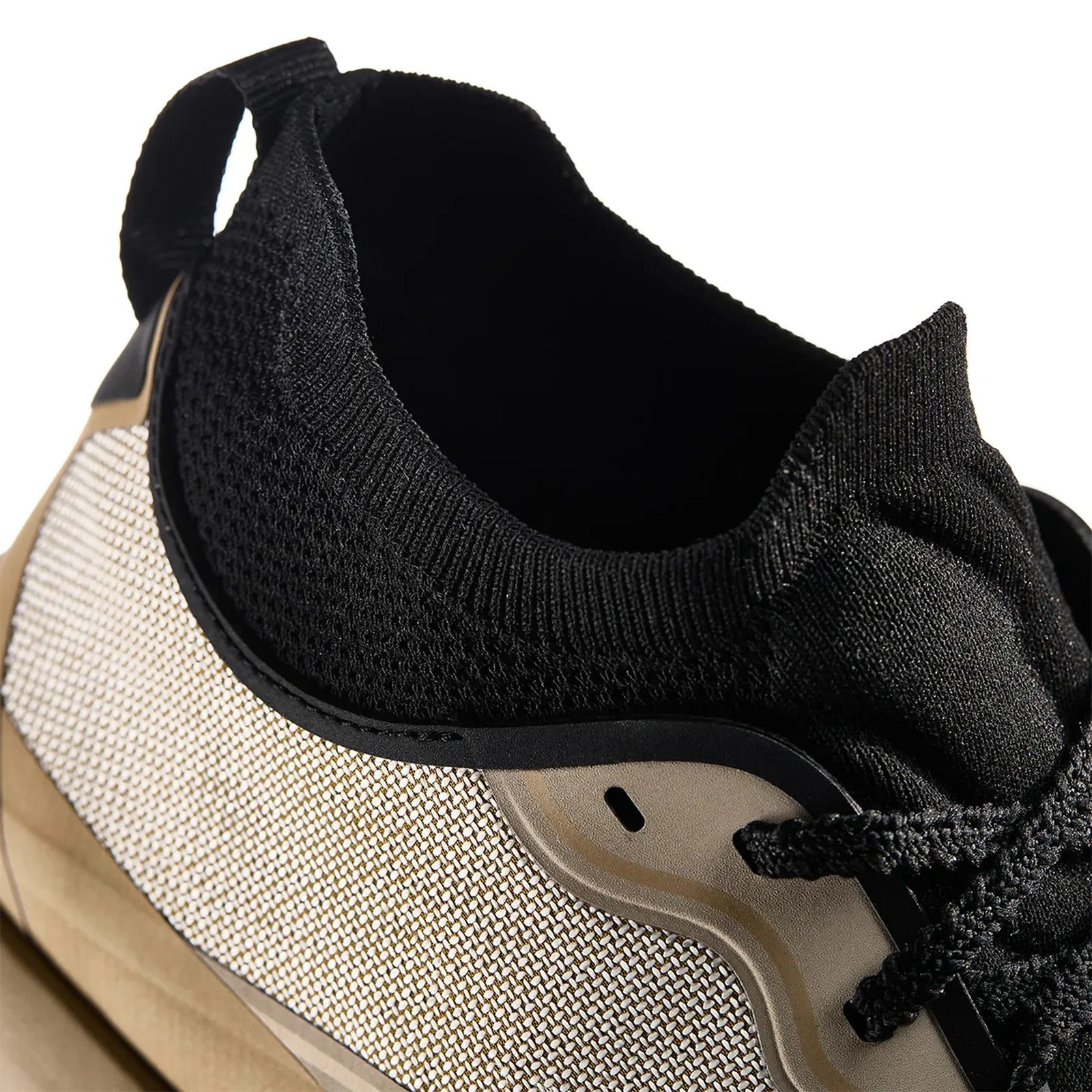 Close-up of a sneaker with black knit collar, beige and white mesh side panel, and black laces.