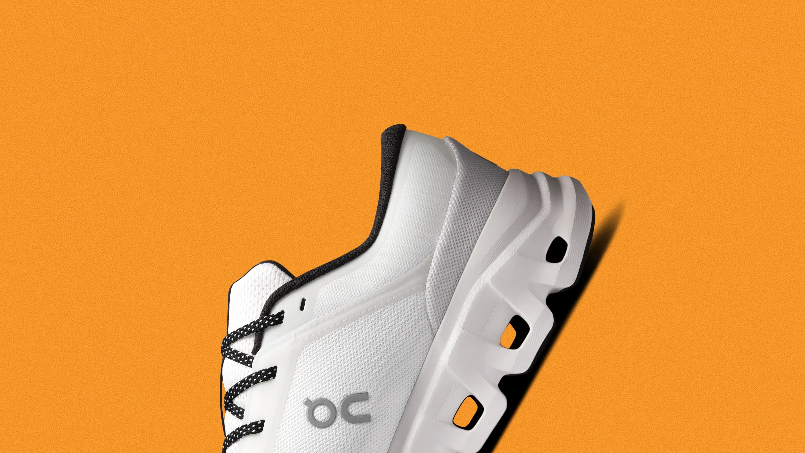 White athletic shoe with black and white laces and a unique segmented sole on an orange background.